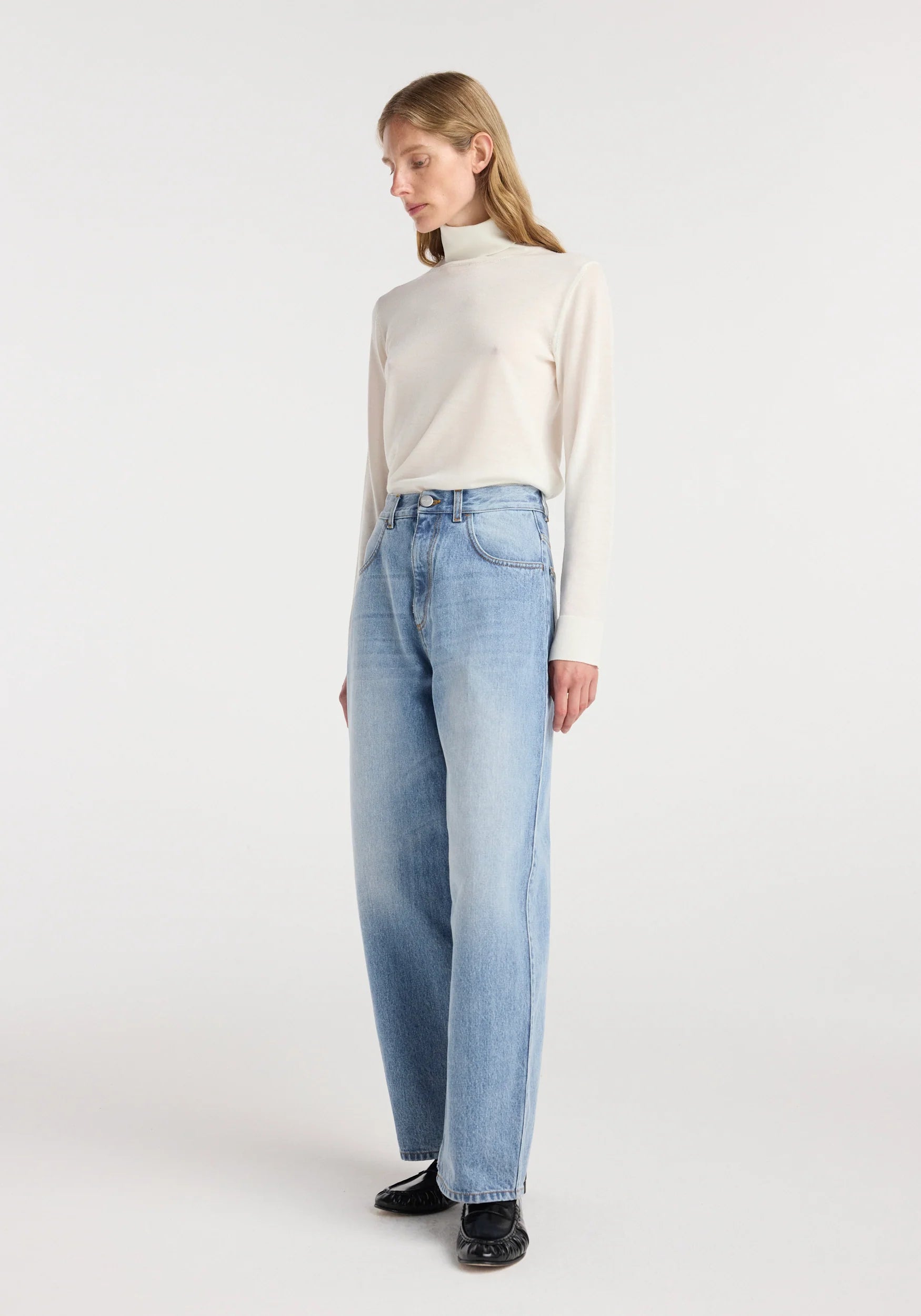Woman wearing a white turtleneck and light blue jeans on a white background