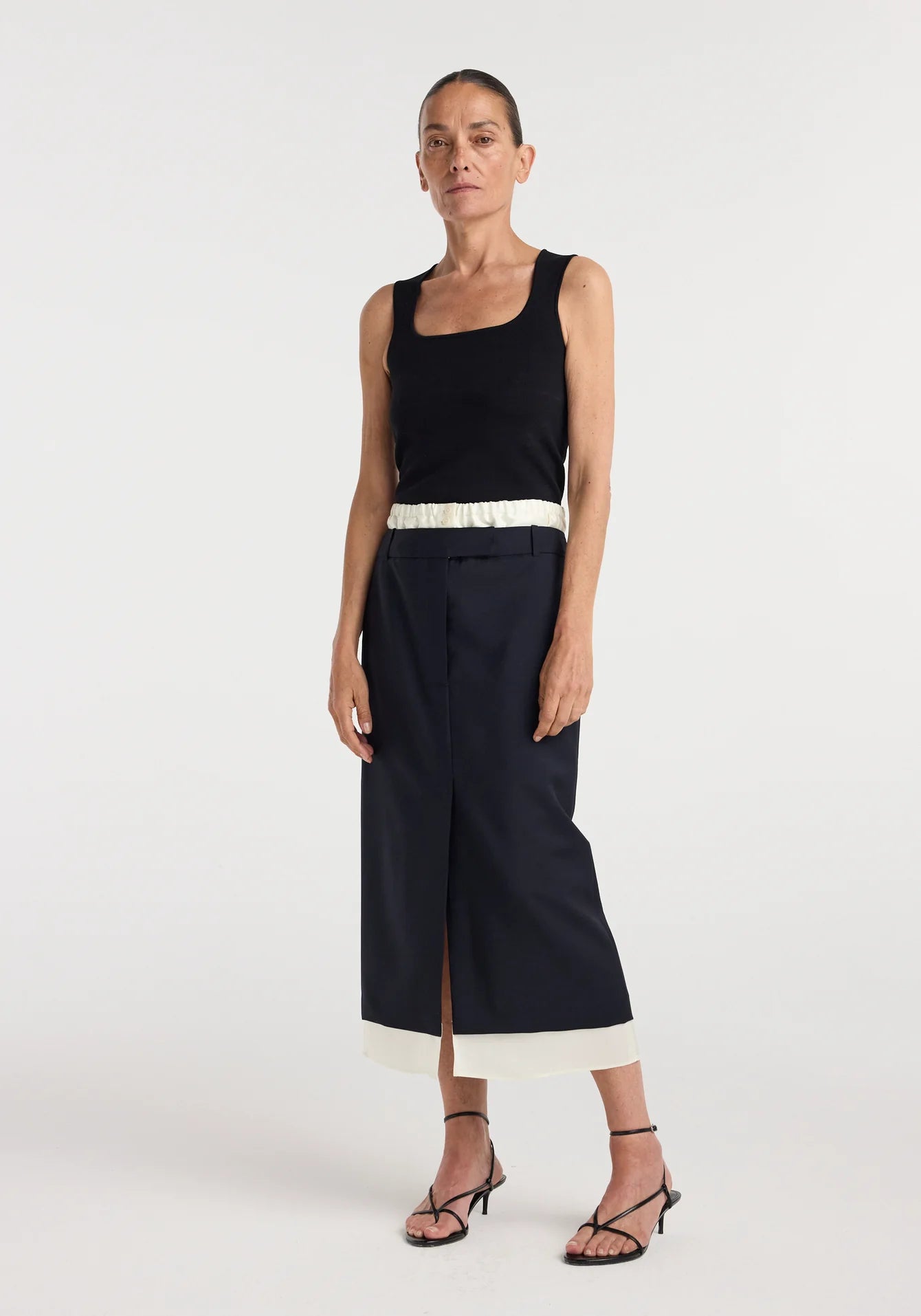 Woman wearing a black sleeveless top and navy pants with a white trim on a white background