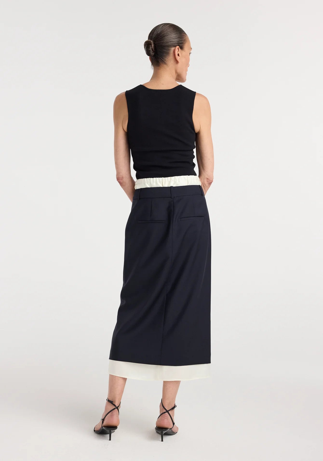 Woman wearing a black sleeveless top and long navy skirt on a white background
