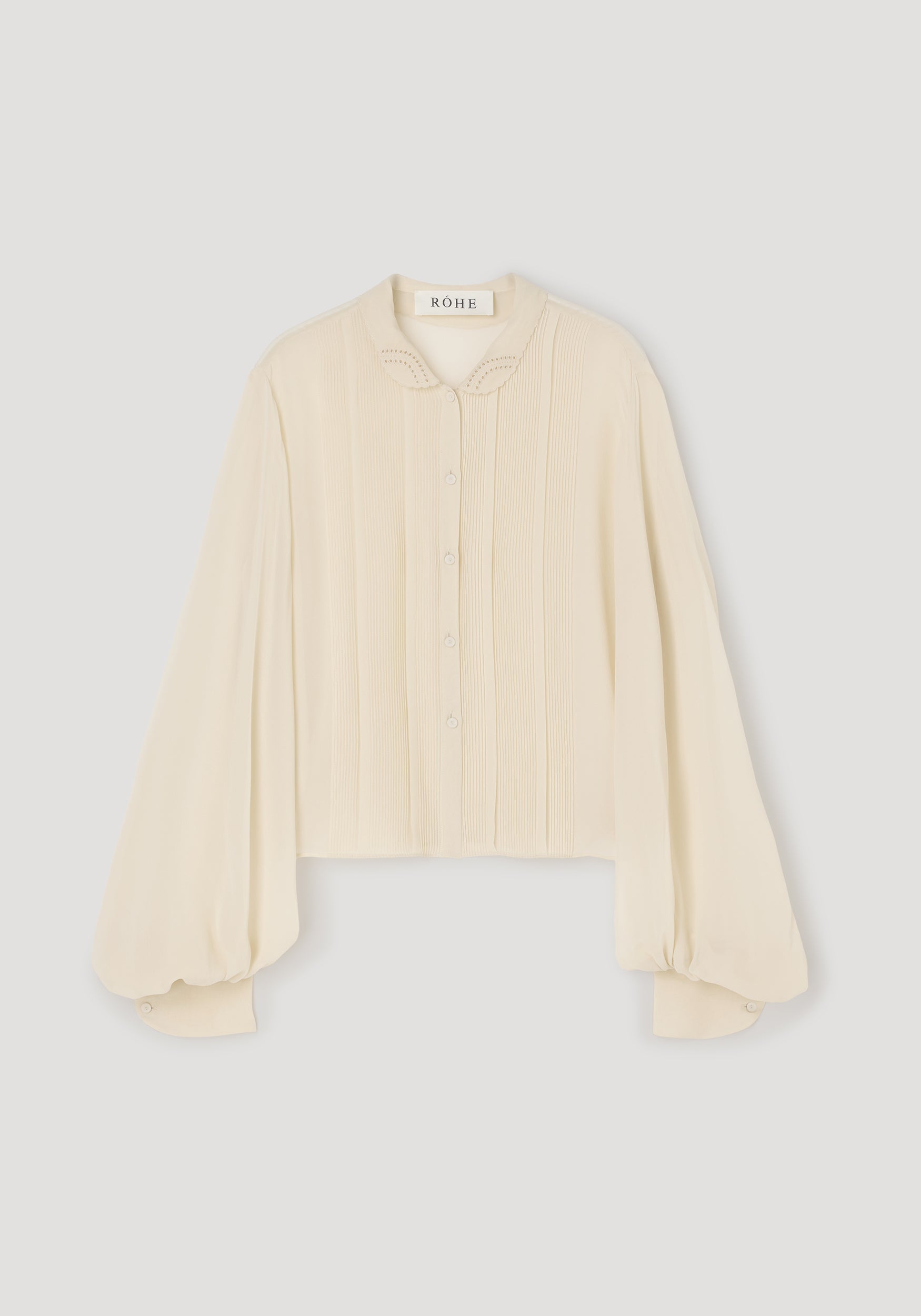 A cream-colored long-sleeve blouse with pleated detailing on the front and a pointed collar, shown flat against a light gray background.