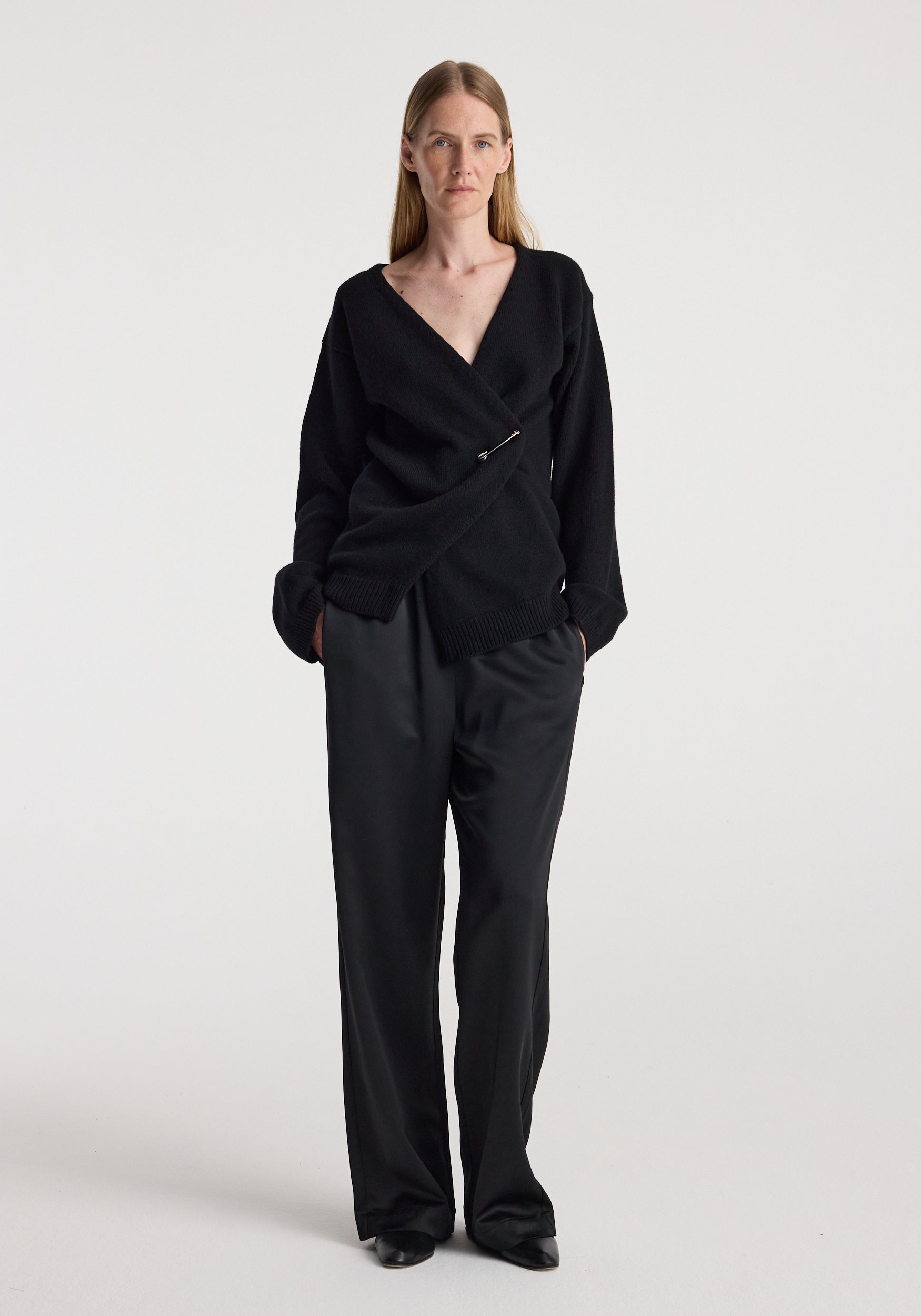 A woman modeling a black wrap-style long-sleeve top and matching black wide-leg trousers against a plain light gray studio background.