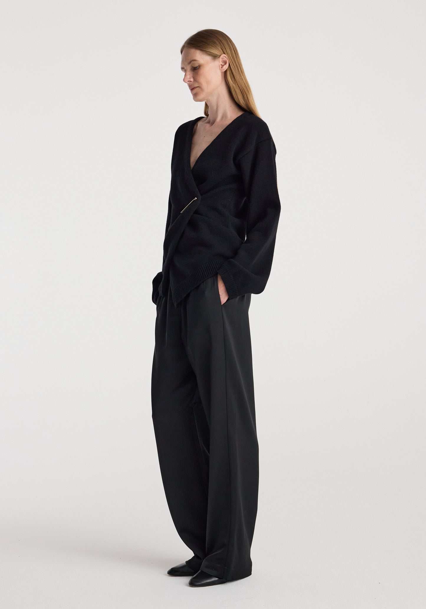 A woman modeling a black wrap-style long-sleeve top and matching wide-leg trousers against a plain light gray studio background.