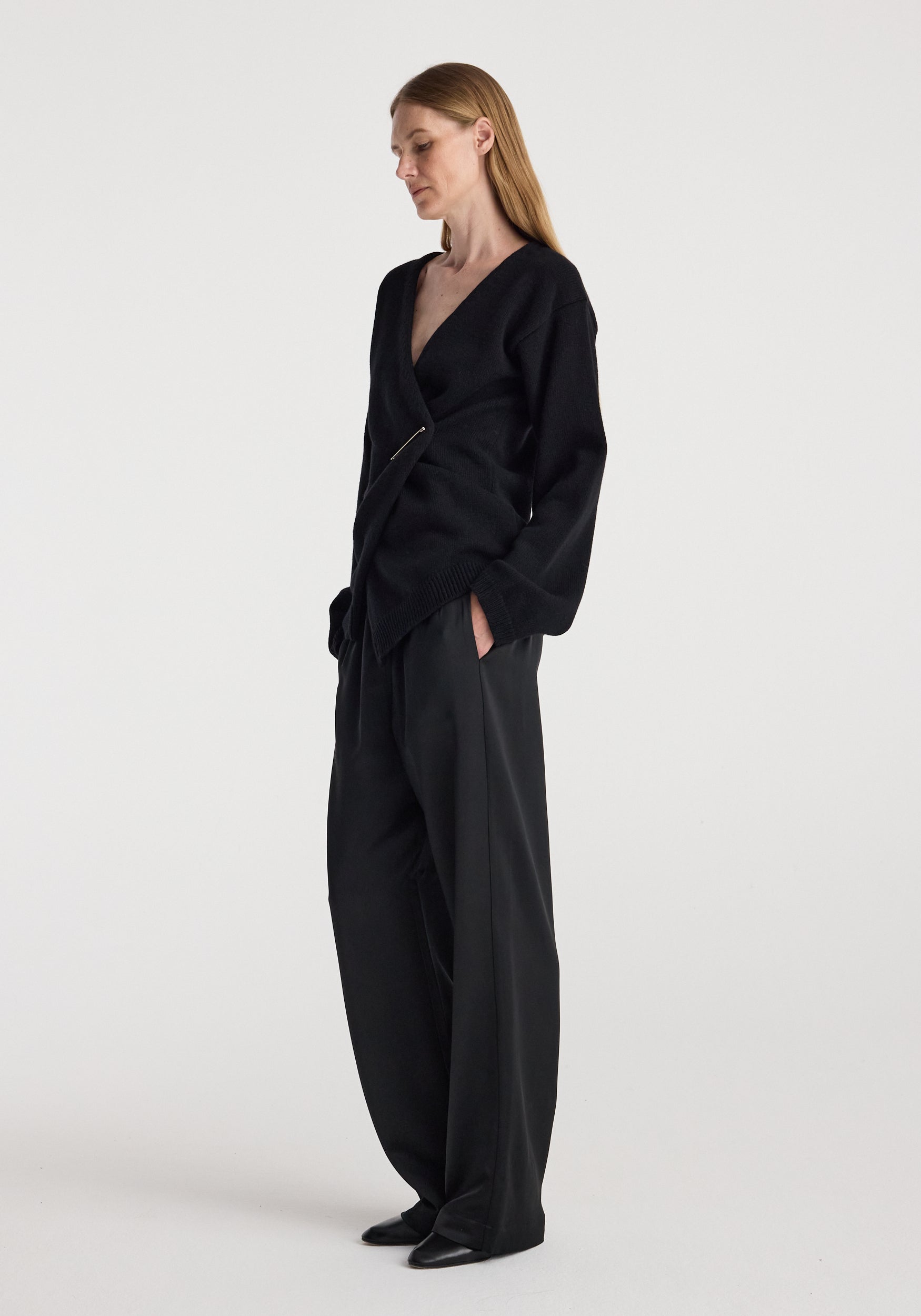 A woman modeling a black wrap-style long-sleeve top and matching wide-leg trousers against a plain light gray studio background.