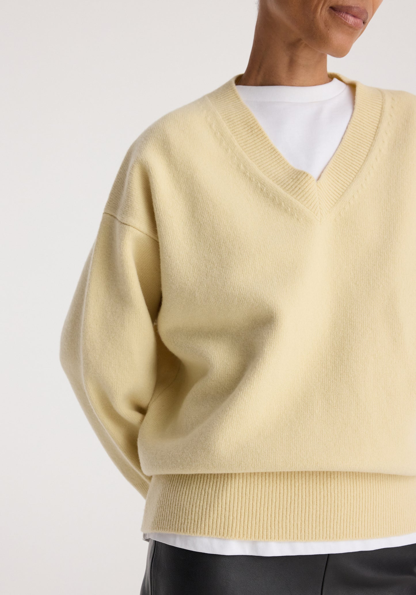 A close-up of a person wearing a pale cream-yellow V-neck knit sweater over a white undershirt, against a plain light background.