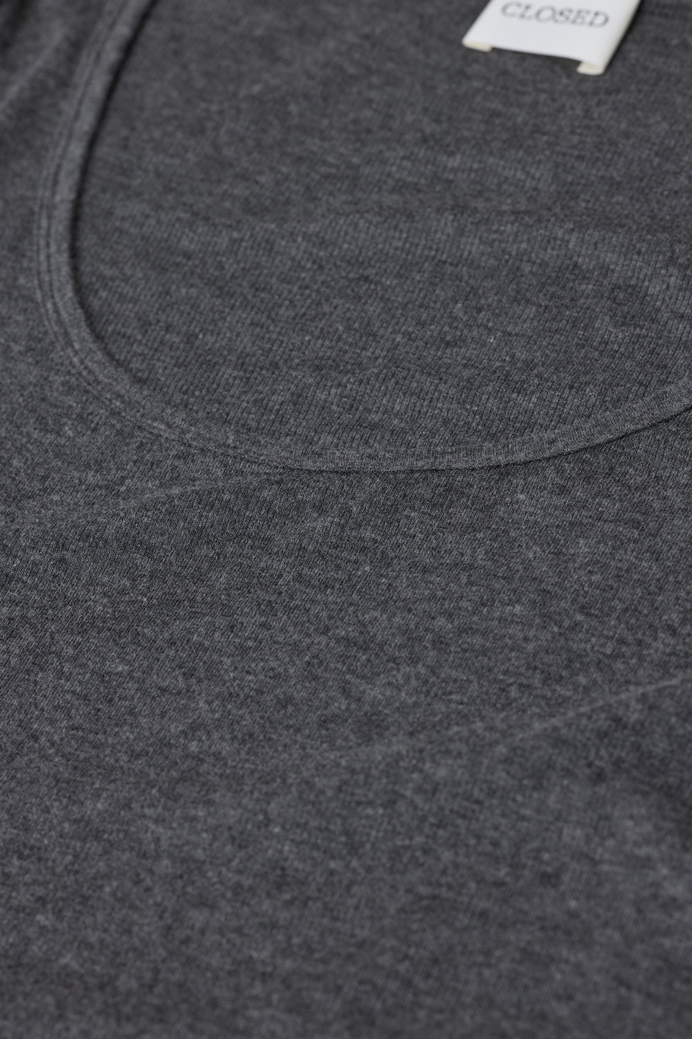 Close-up of a dark gray heather knit garment, showing the texture of the fabric and a small white tag near the neckline.