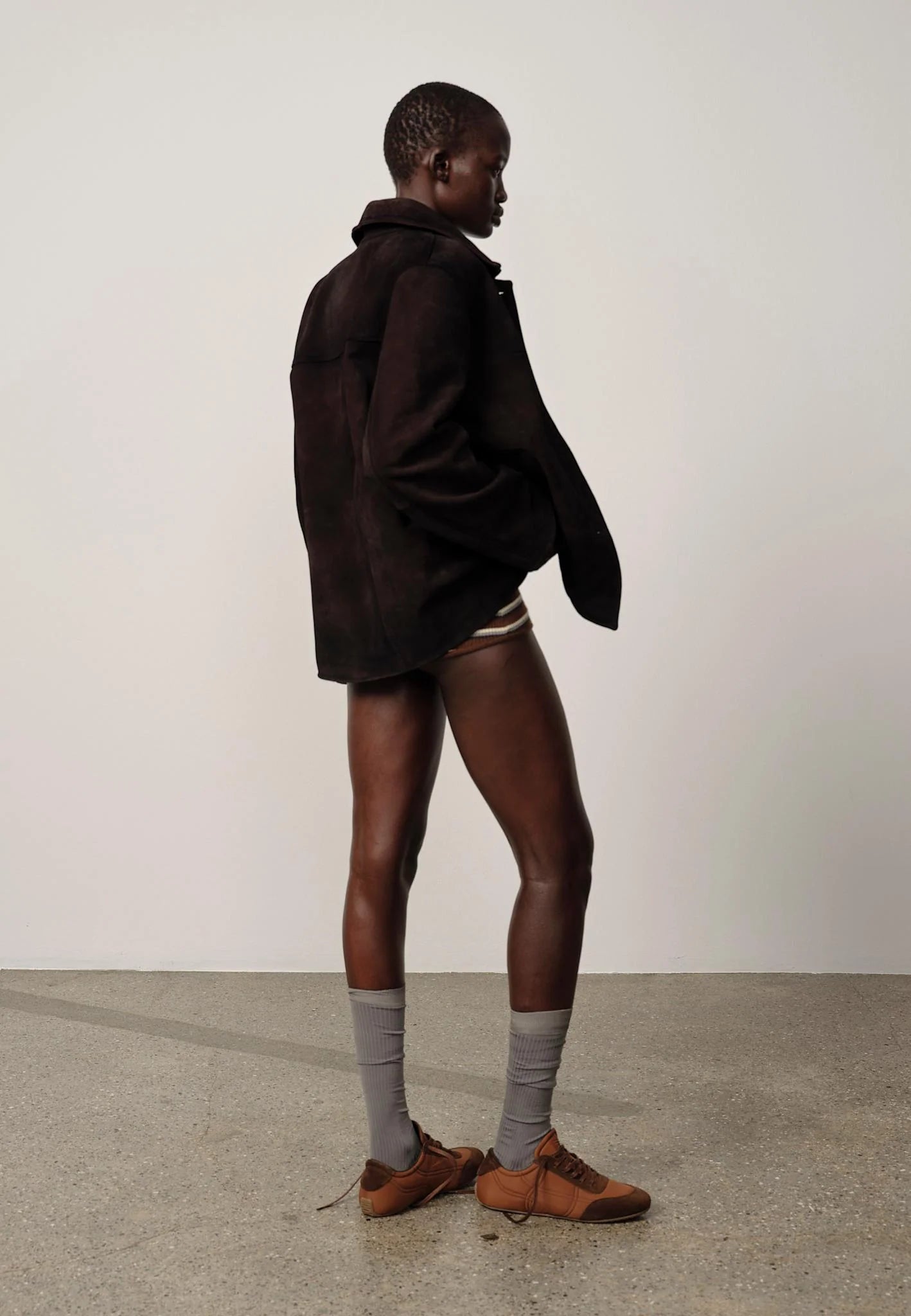 Person wearing a dark coat, shorts, and gray socks standing against a plain background