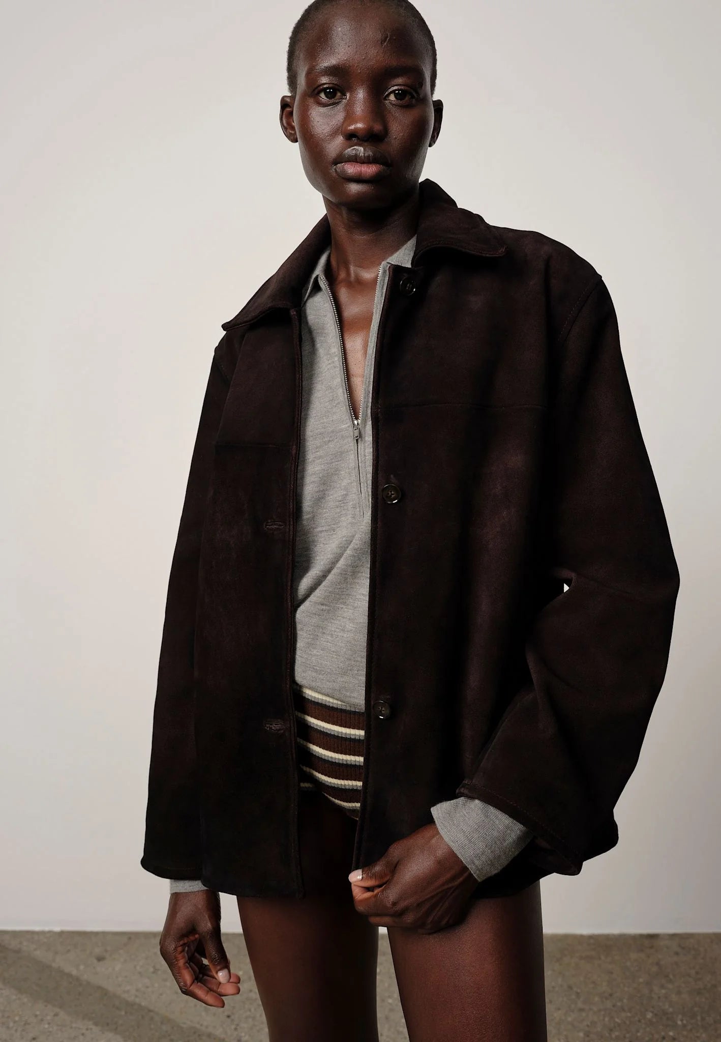 Person wearing a dark brown jacket over a light shirt with a plain background