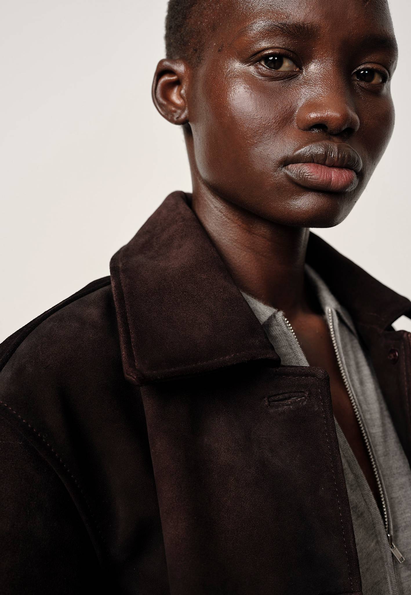 Person wearing a dark brown suede jacket against a neutral background