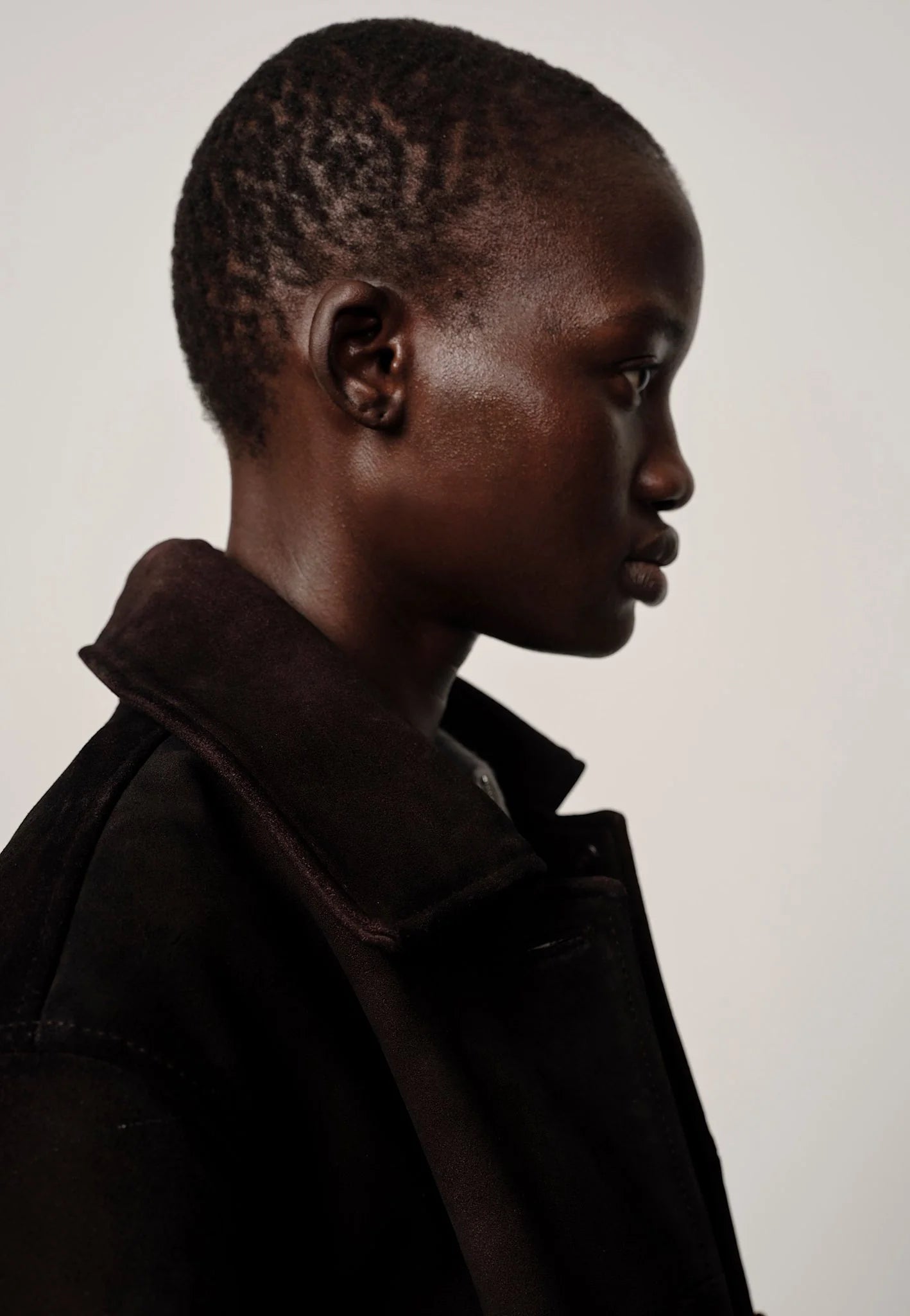Side profile of a person wearing a dark coat against a plain background