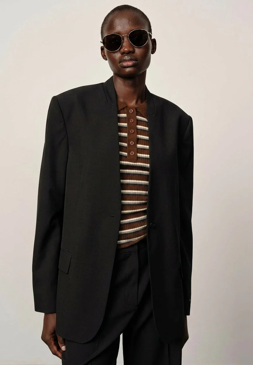 Person wearing a black blazer over a striped shirt on a plain background