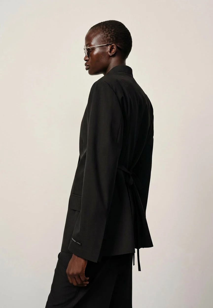 Person wearing a black suit against a plain background