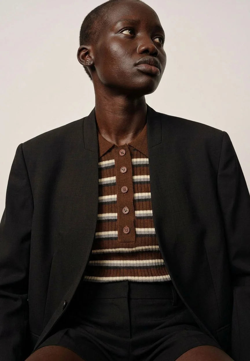 Man wearing a dark blazer over a striped shirt with a plain background