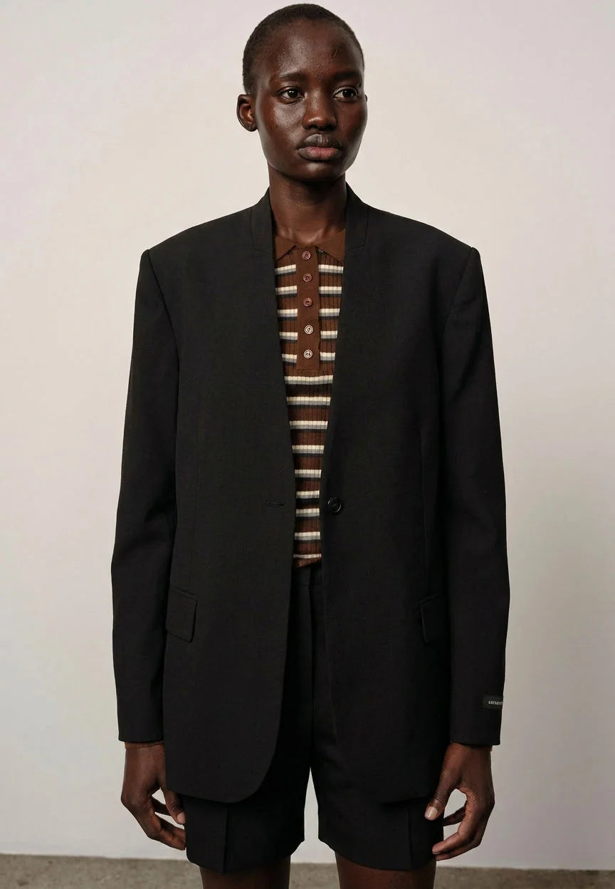 Person wearing a black suit with a striped shirt against a plain background