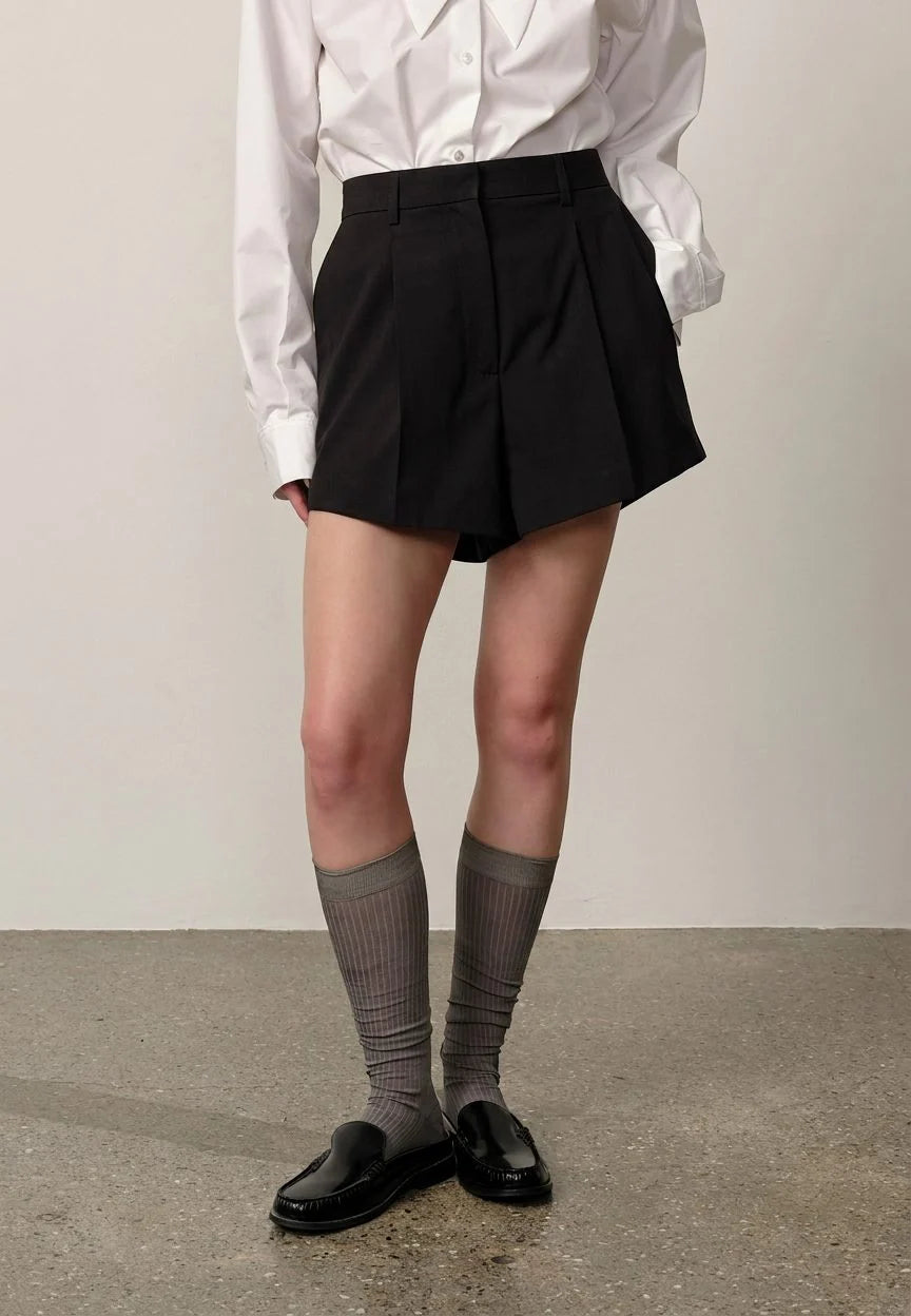 Person wearing a white shirt, black pleated skirt, gray socks, and black shoes on a plain background