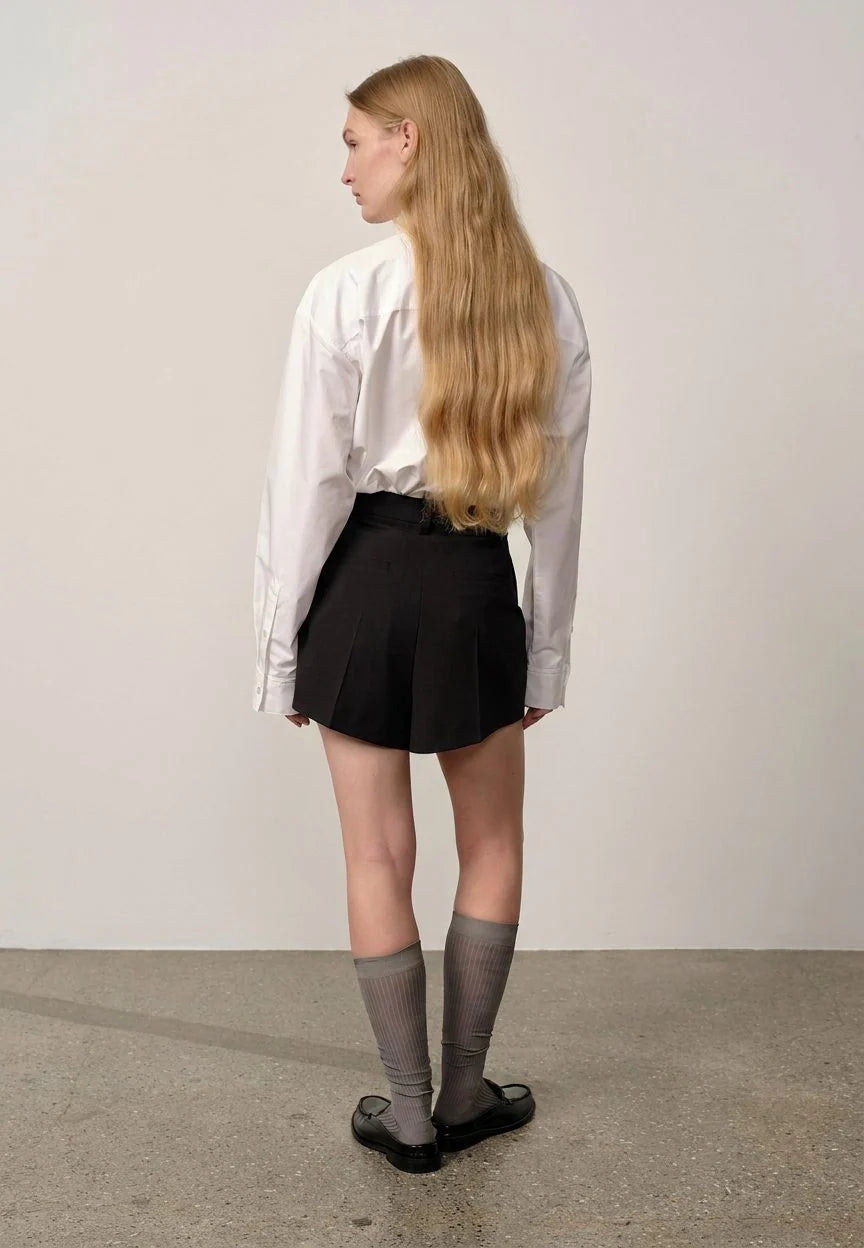 Person wearing a white shirt, black skirt, and knee-high socks standing against a plain background