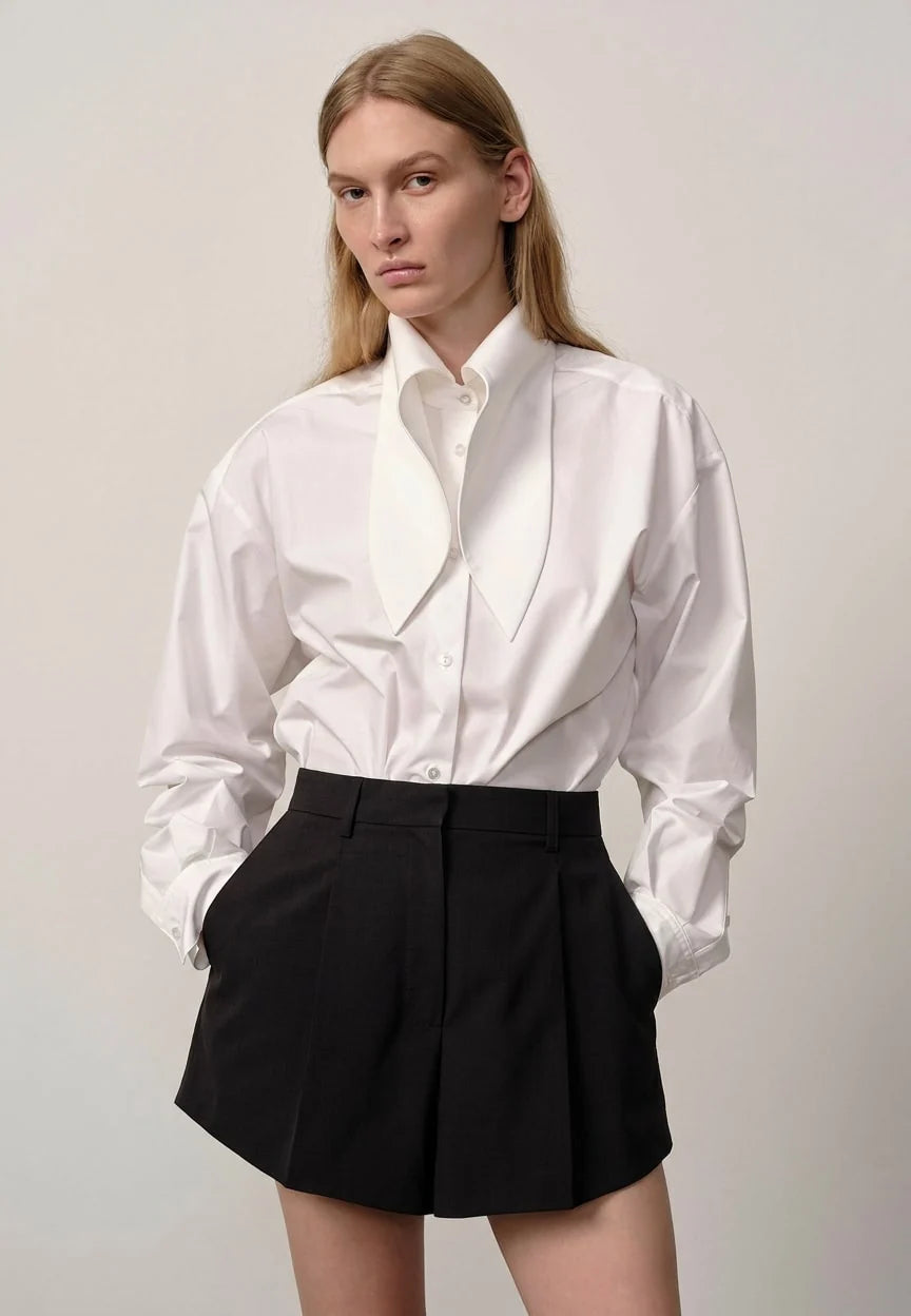 Person wearing a white shirt and black shorts against a plain background