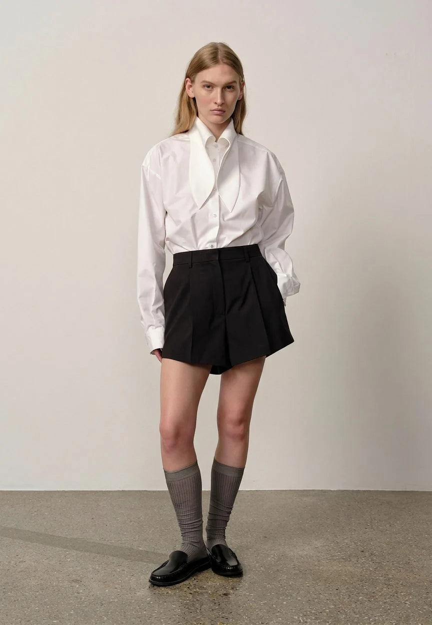 Person wearing a white shirt, black shorts, and gray socks against a plain background