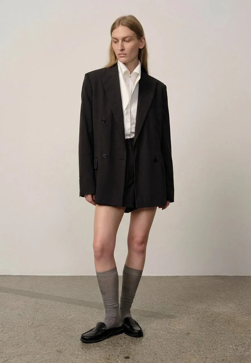 Person wearing a black blazer, white shirt, and gray knee-high socks against a plain background