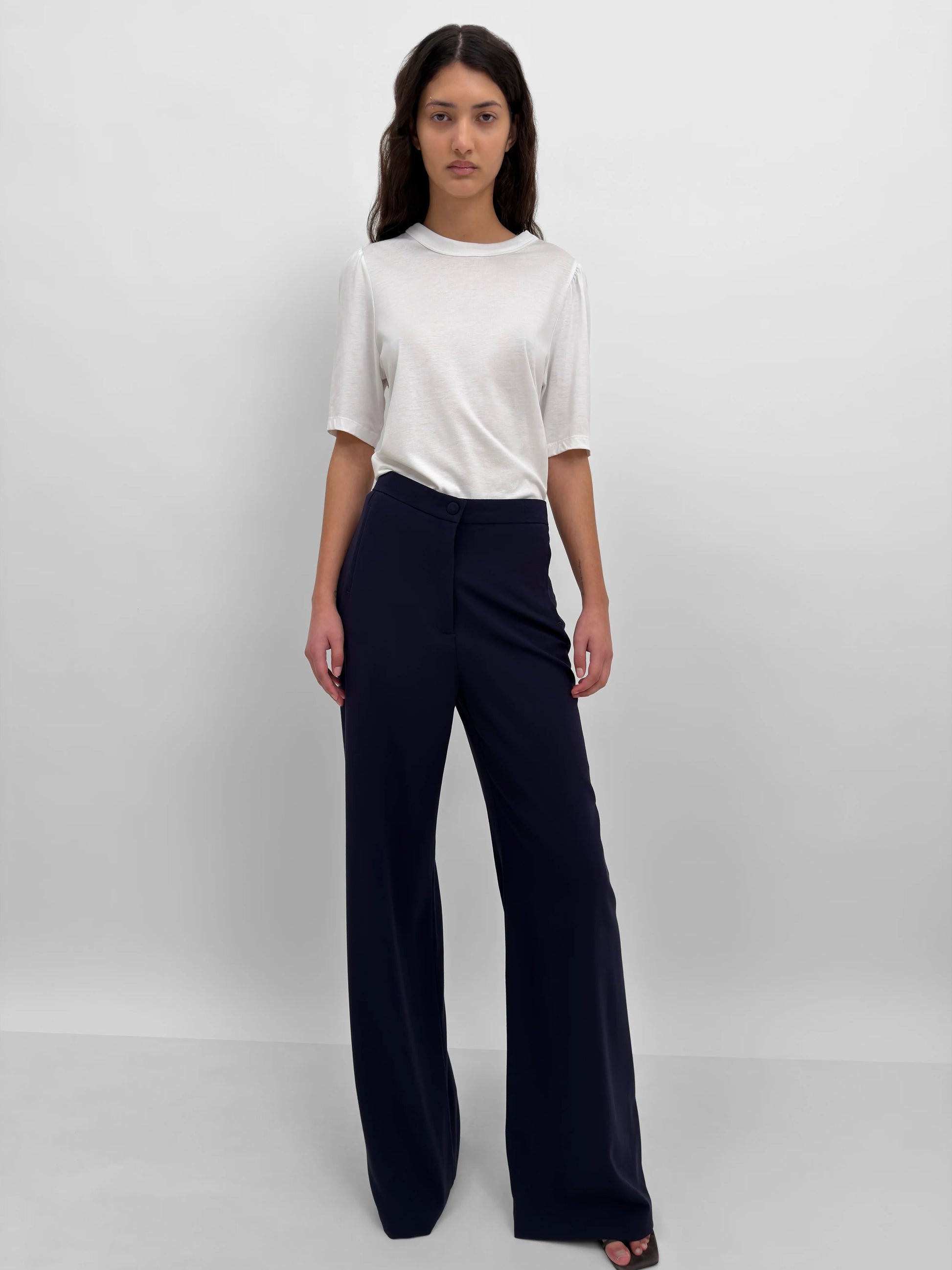 Woman wearing a white top and navy pants on a plain background