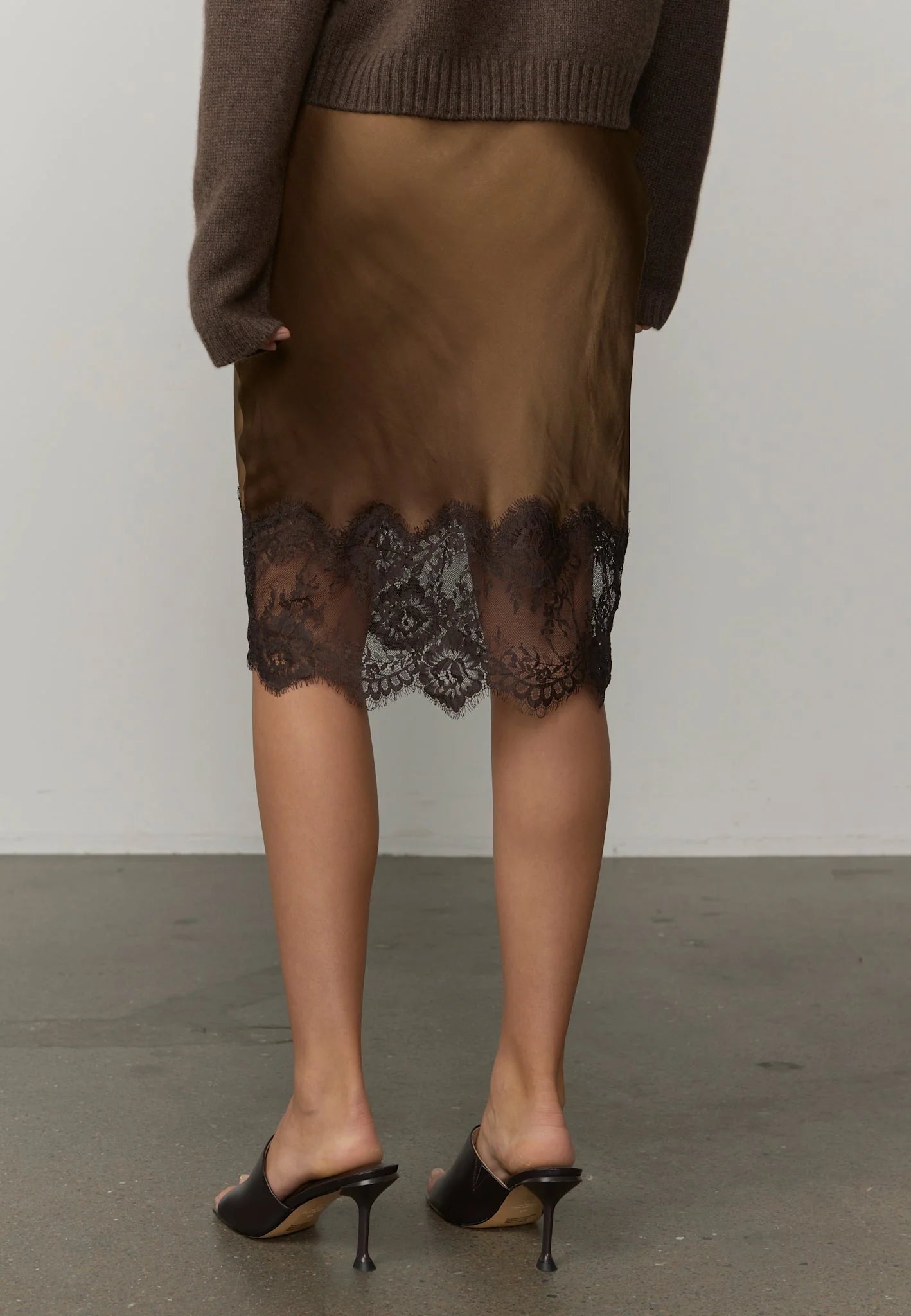 Person wearing a brown skirt with lace details and a brown sweater, standing against a plain background.