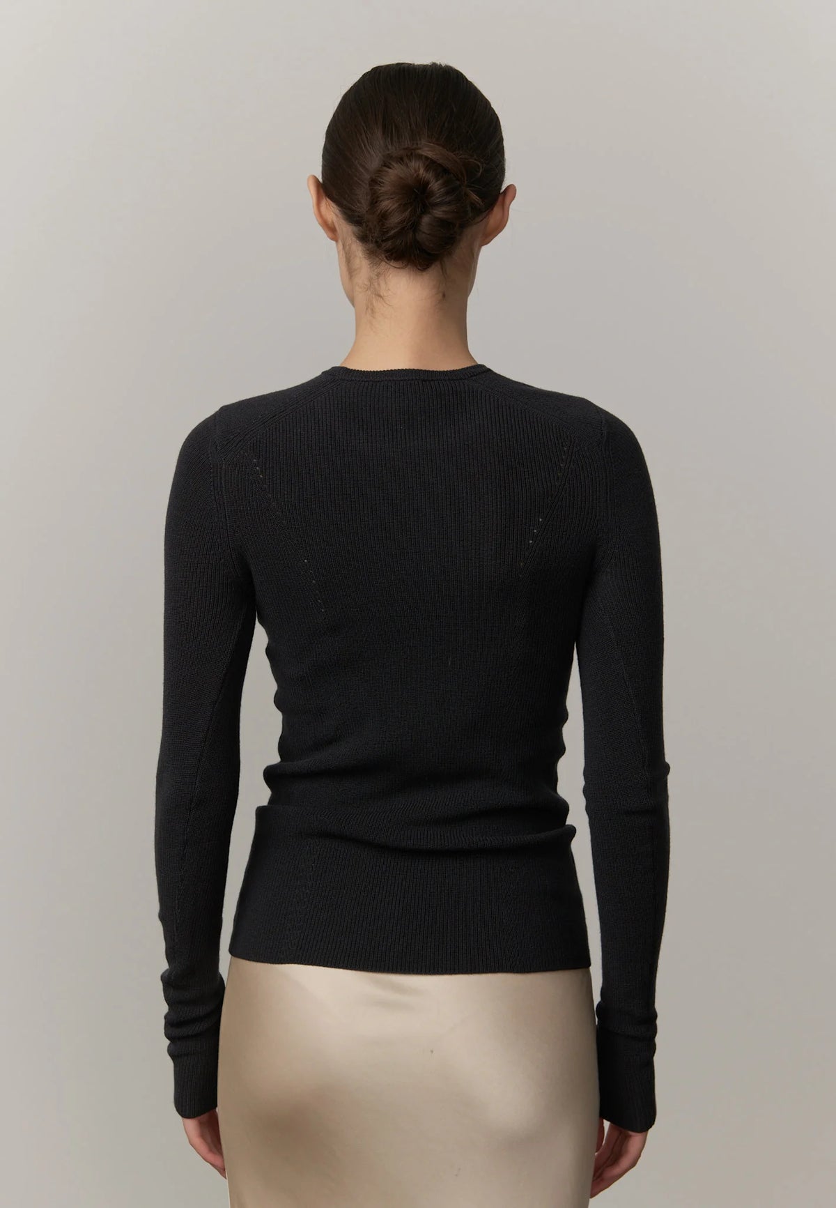 Person wearing a black long-sleeve top against a neutral background
