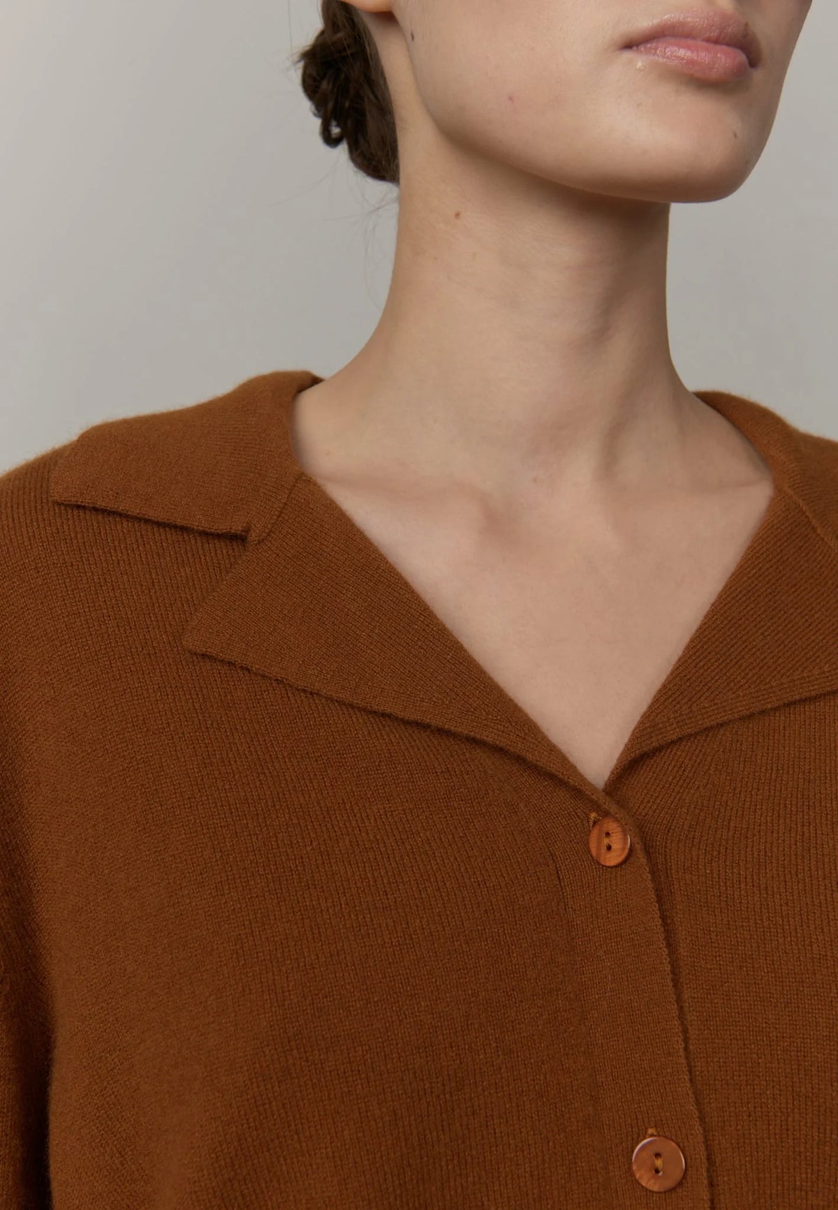 Close-up of a model wearing a brown knit cardigan with a collar and brown buttons against a neutral light gray background.