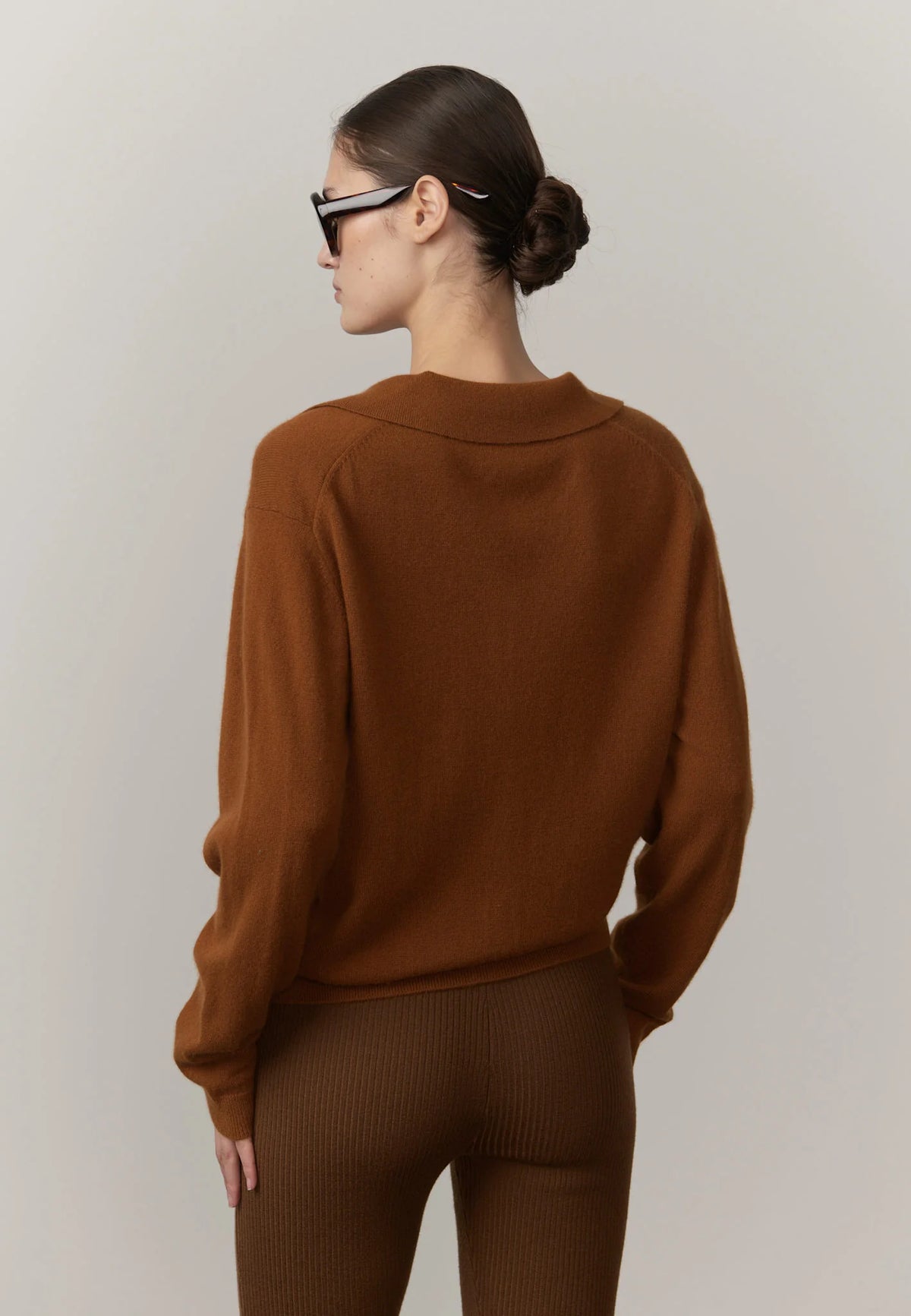 Person wearing a brown sweater and pants against a plain background