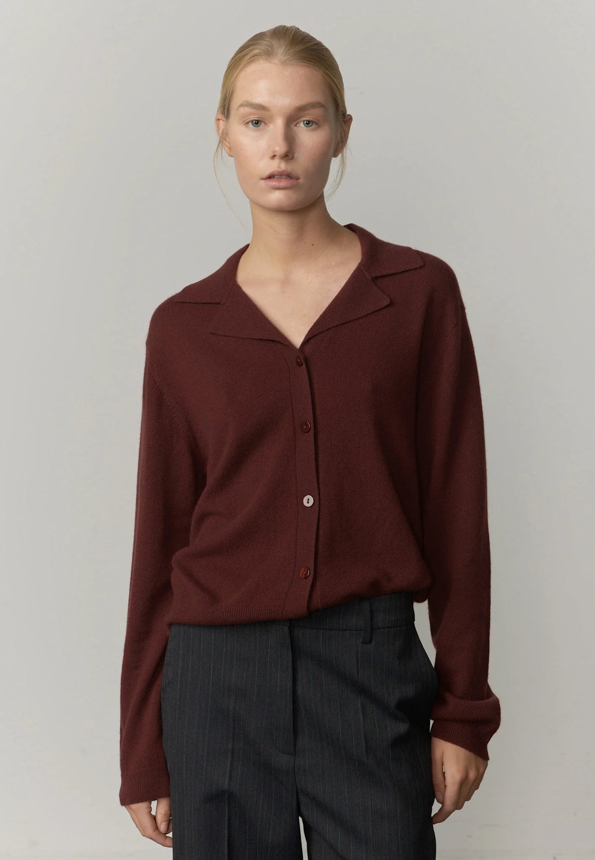 Woman wearing a burgundy shirt and dark pants against a plain background