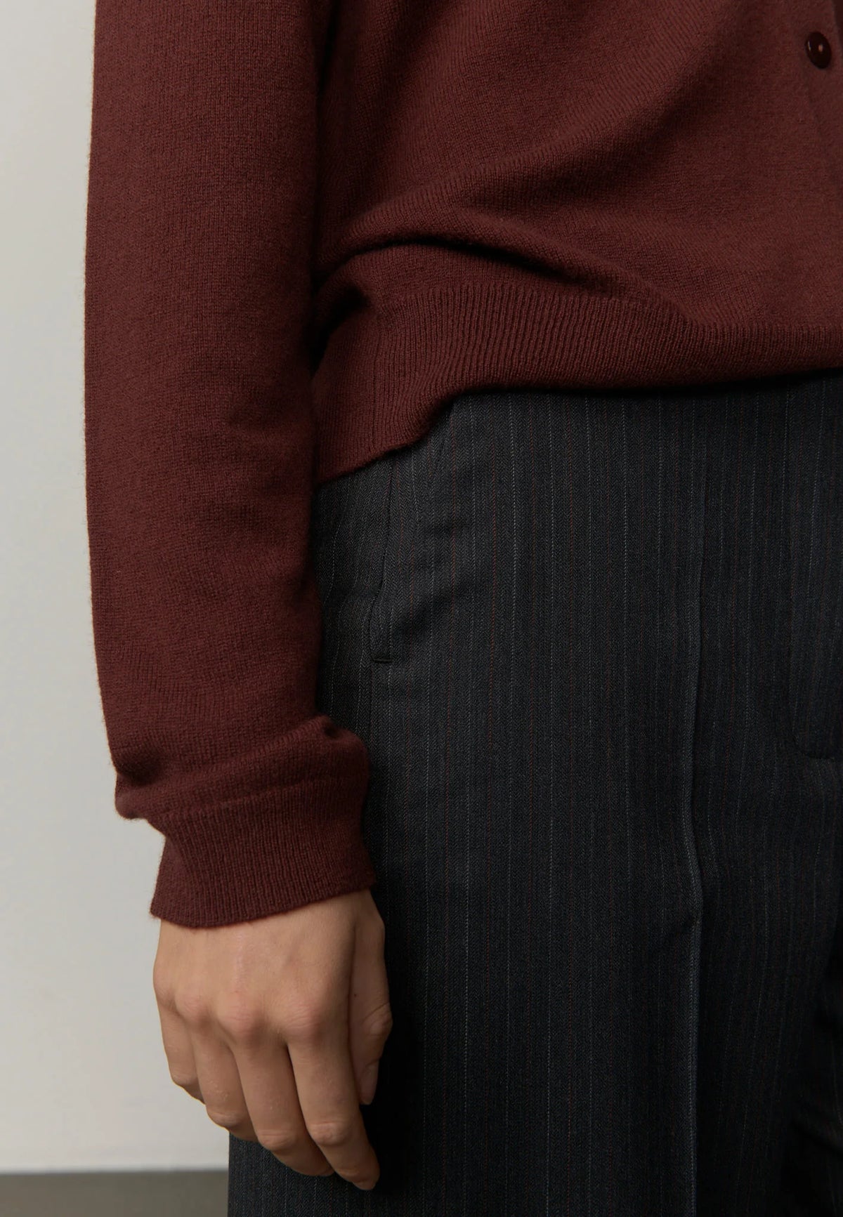Person wearing a burgundy sweater and dark pants against a plain background