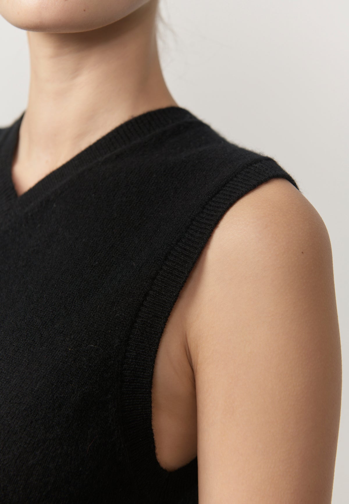 Close-up of a person wearing a black sleeveless knit top, showing the shoulder, neck, and upper chest against a plain light background.