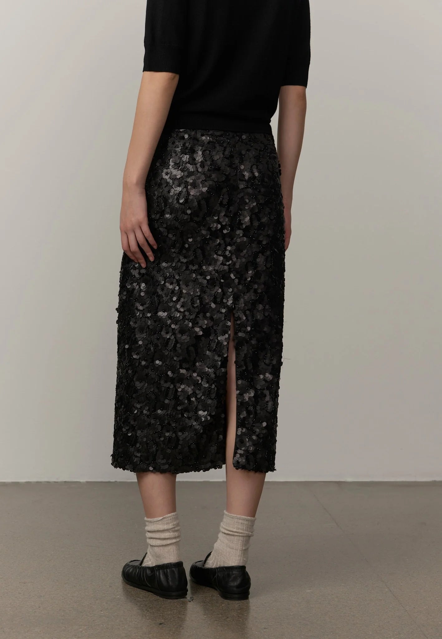 Person wearing a black sequin skirt with a plain background