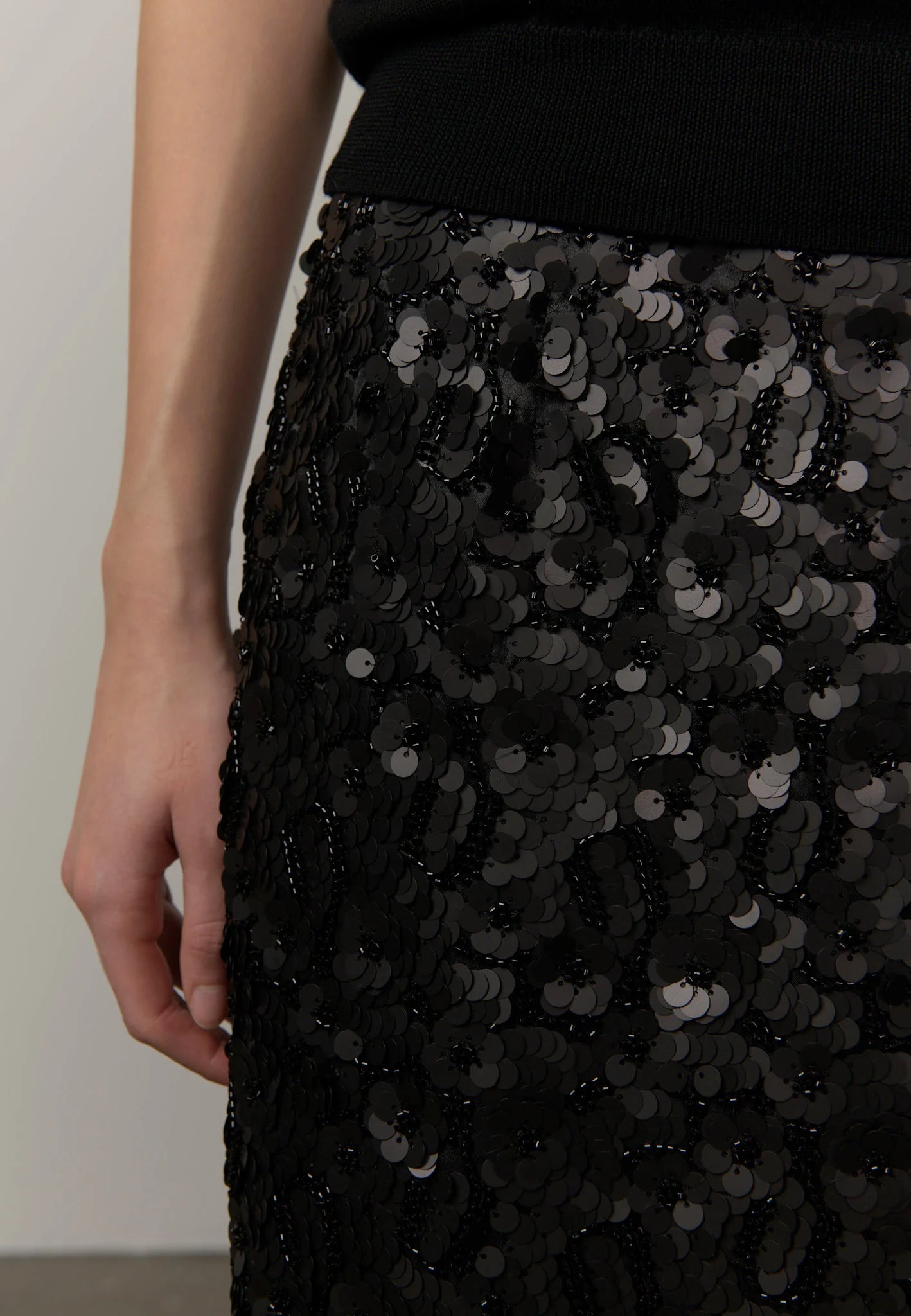 Close-up of a black sequined skirt with a black ribbed top, showing a person's hand and torso against a plain light background.