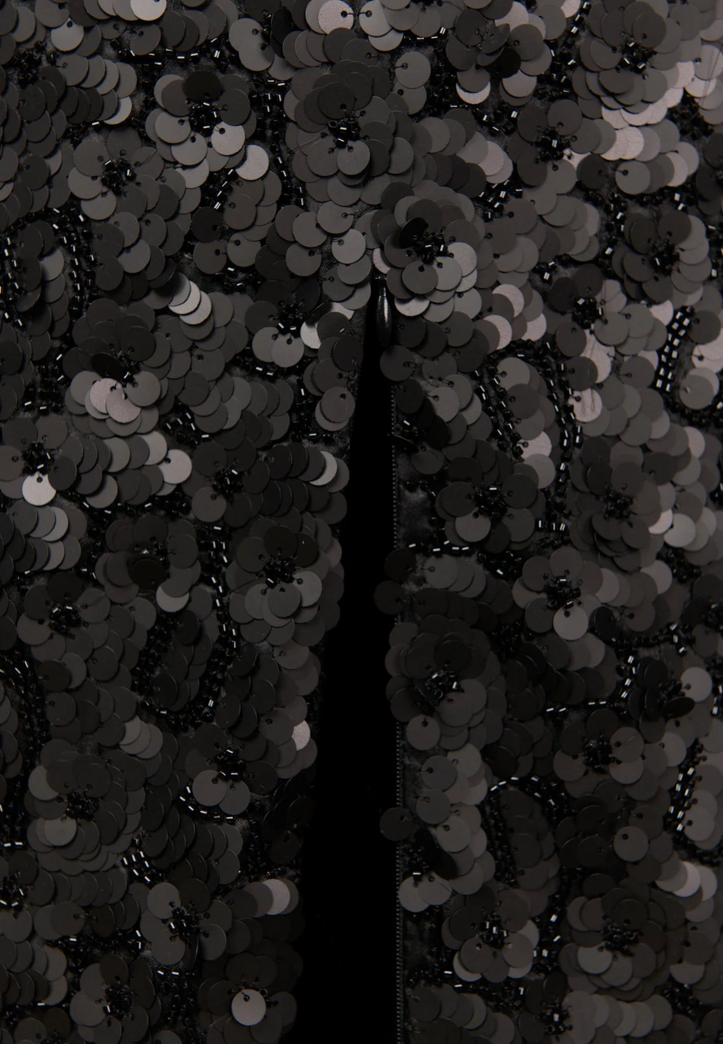 Close-up of a black sequined fabric with overlapping round sequins and a central vertical opening showing a dark interior.