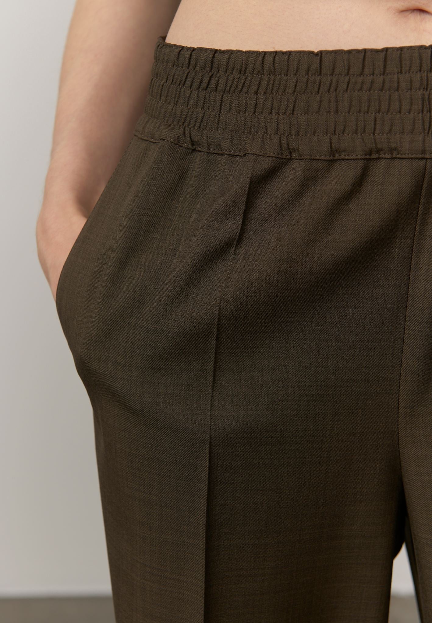 Close-up of a person wearing dark brown textured trousers with an elastic waistband, showing the side pocket and fabric detail.