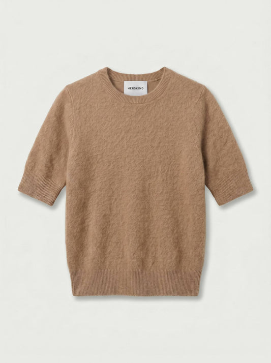 A short-sleeve crewneck knit sweater in a warm camel brown color, displayed flat against a light off-white background. The brand name 'MEEKINS' is visible on the inner neck label.