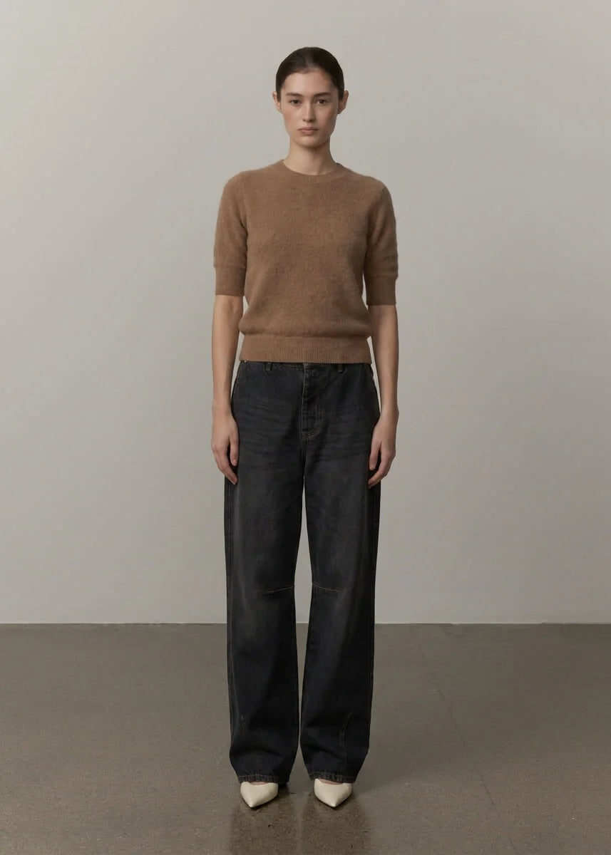 A model stands facing forward in a studio setting, wearing a short-sleeve brown knit sweater and dark wide-leg jeans with white pointed shoes.