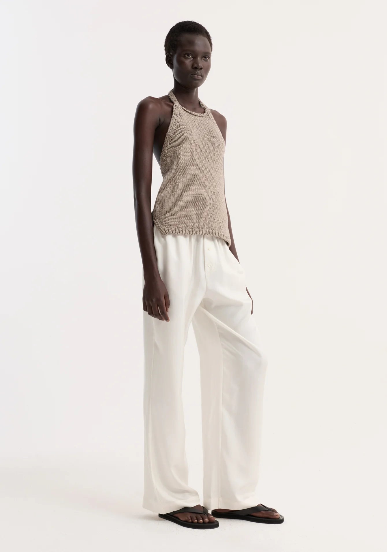 Person wearing a beige sleeveless top and white pants on a white background