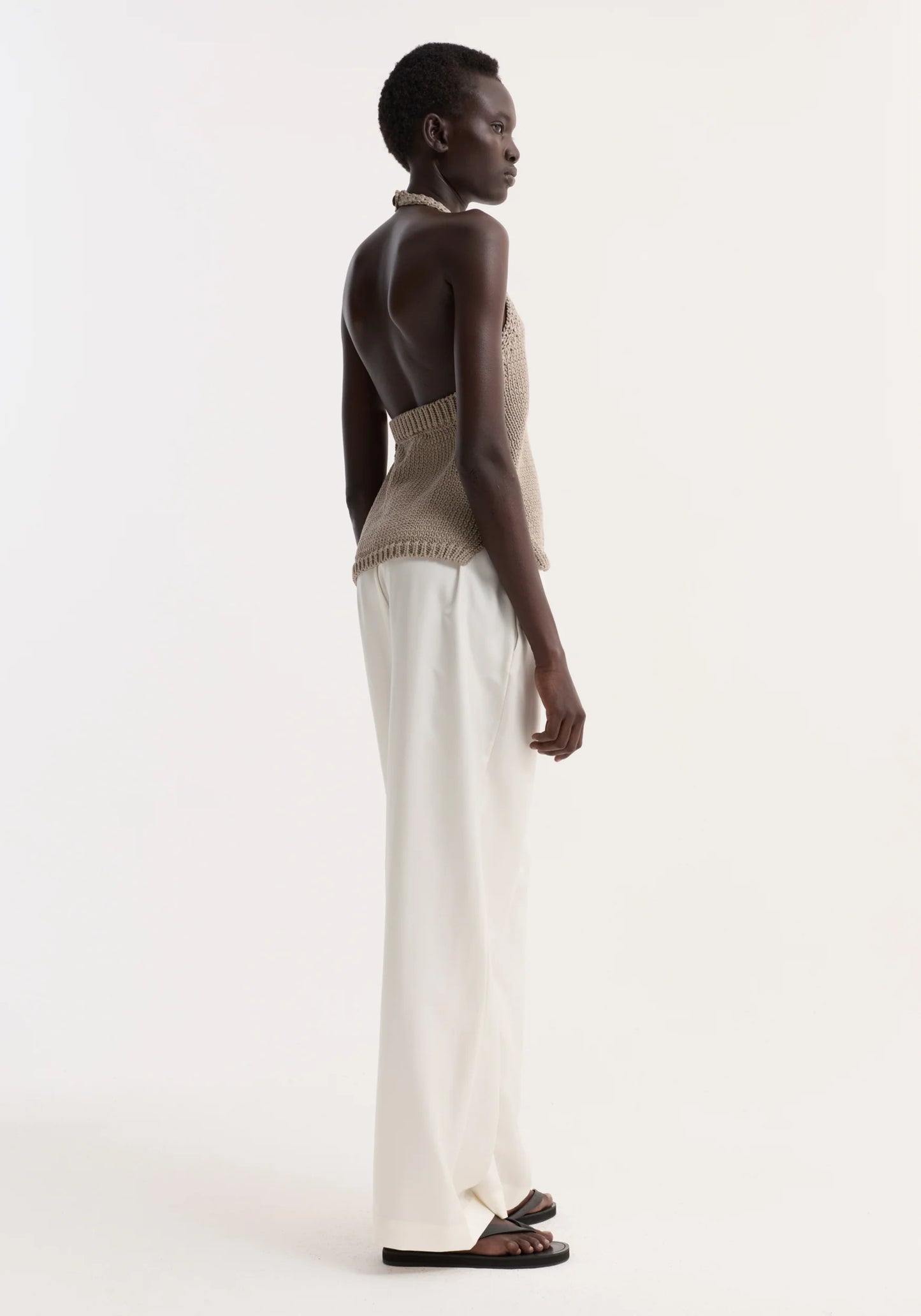 Woman wearing a beige knitted top and white pants on a white background