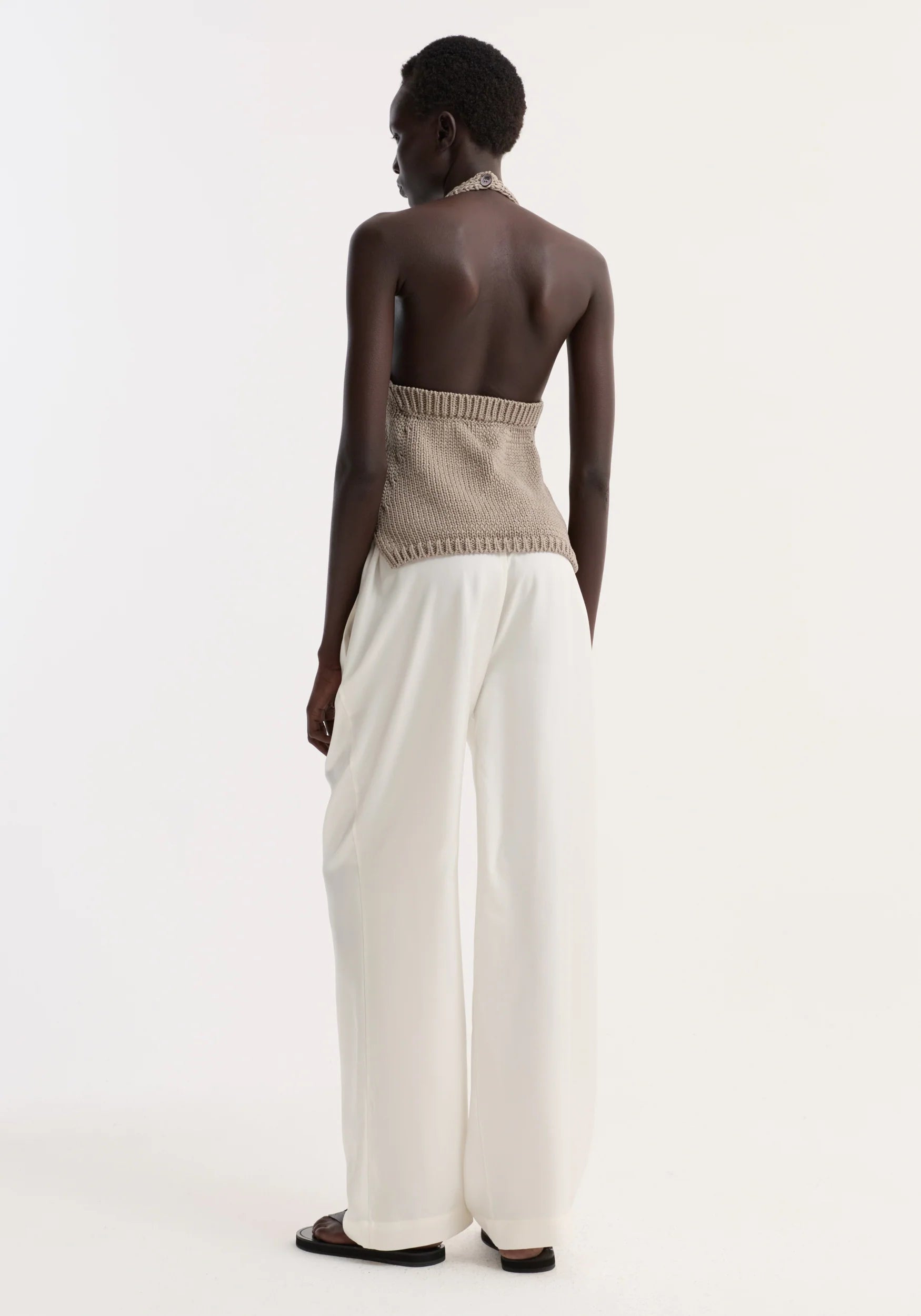 Person wearing a beige strapless top and white pants on a plain background