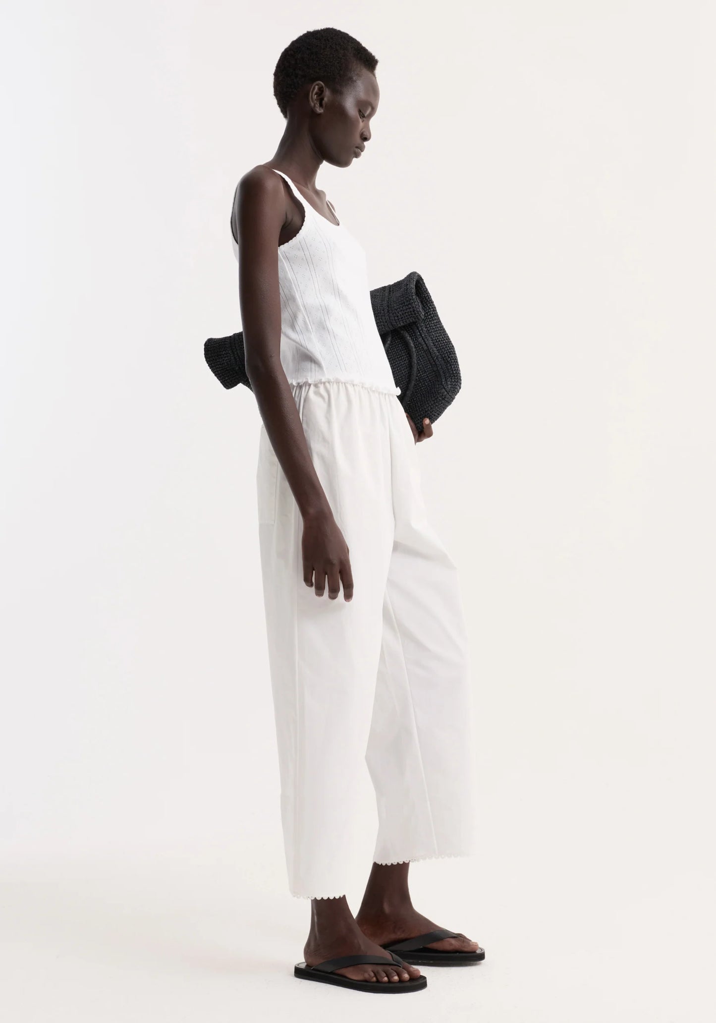 Person wearing a white sleeveless top and pants with a black bag on a white background