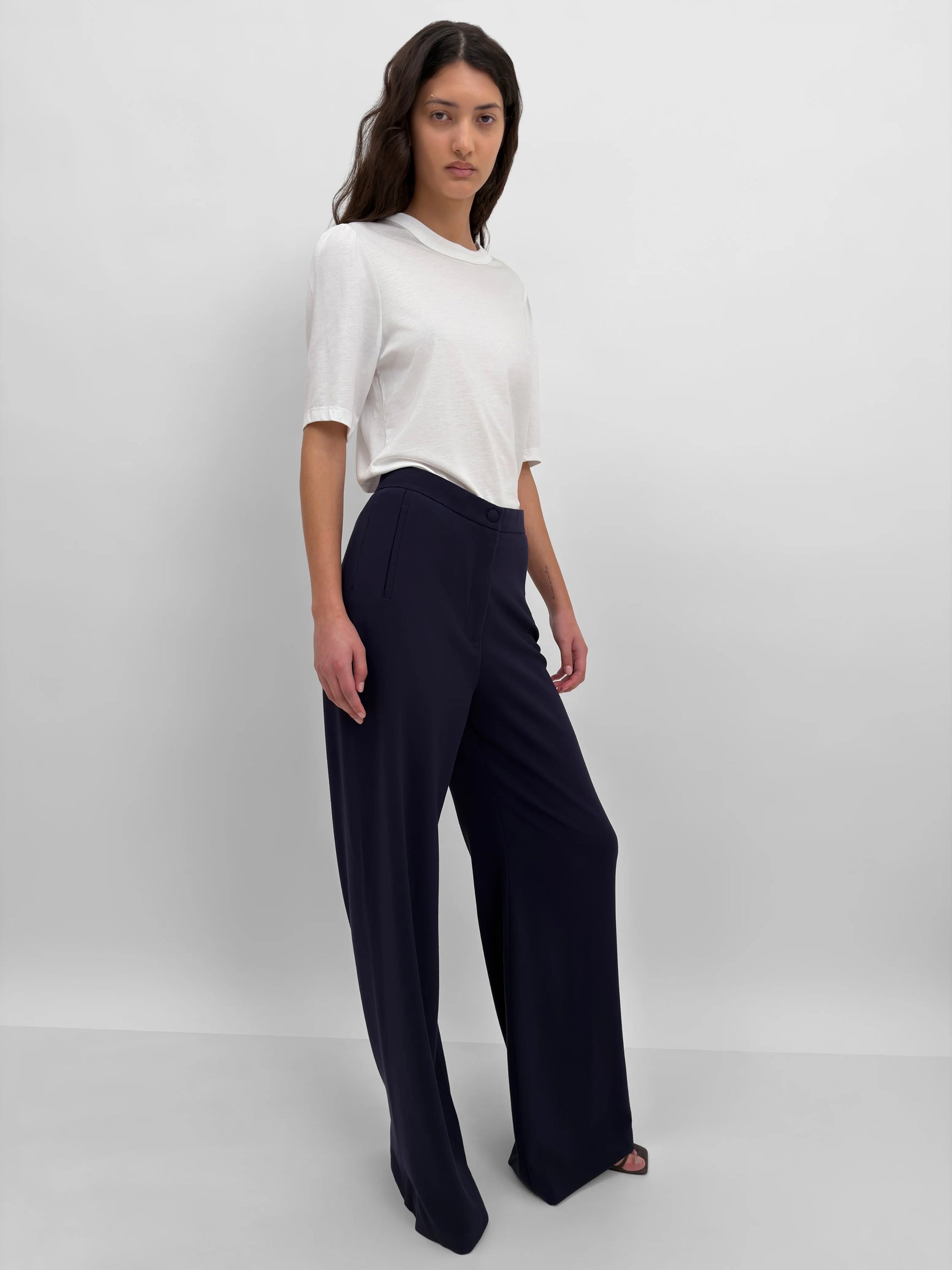 Woman wearing a white top and navy pants on a plain background