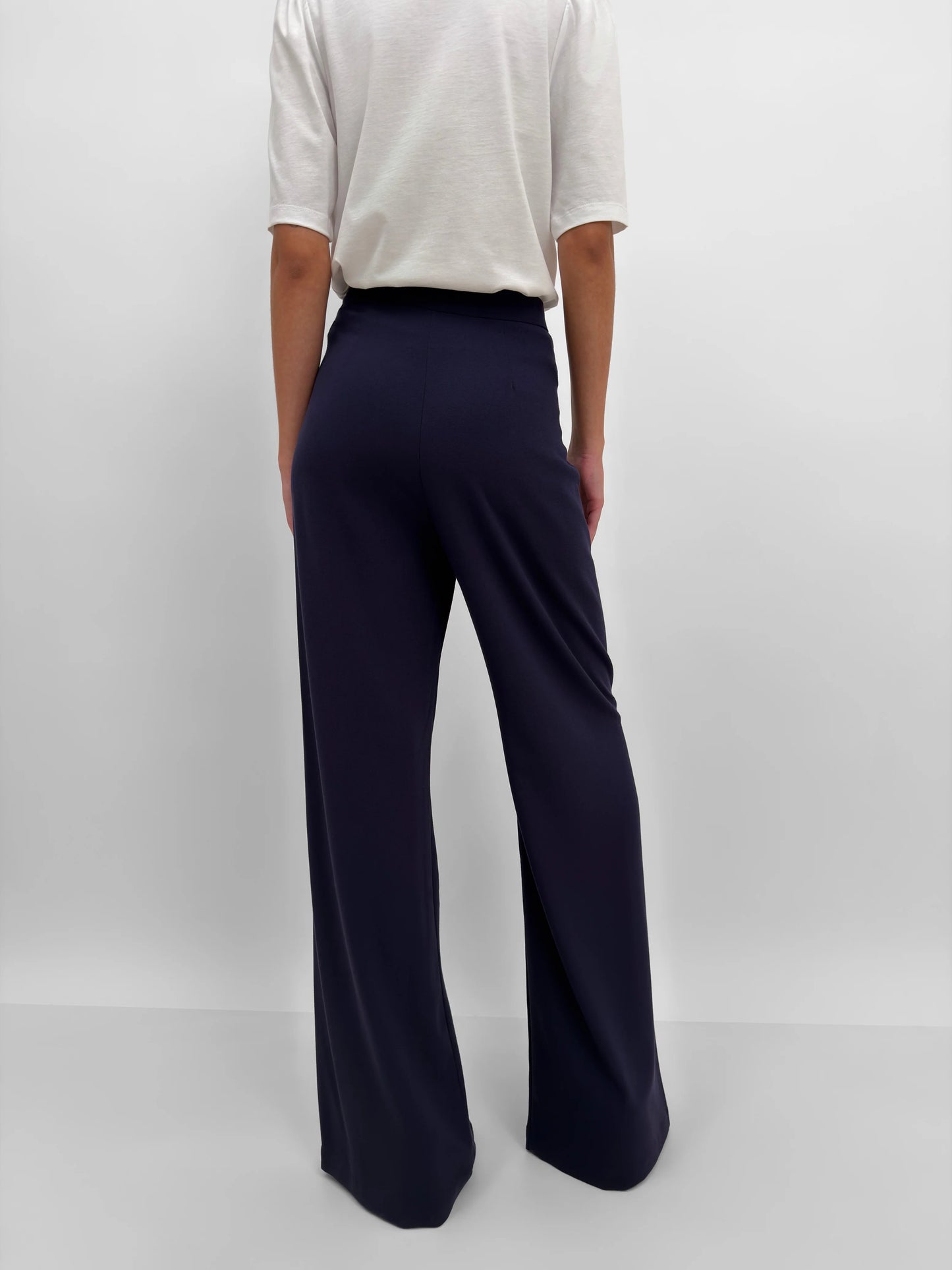 Person wearing navy wide-leg pants and a white top on a plain background