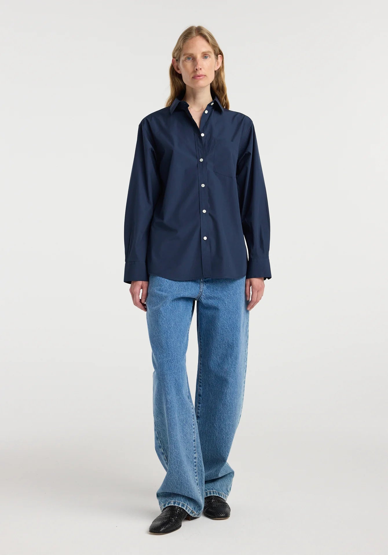 Person wearing a navy blue shirt and blue jeans on a white background