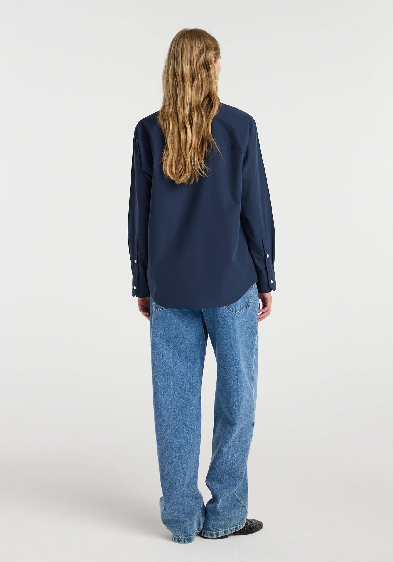 Person wearing a navy blue shirt and blue jeans on a white background