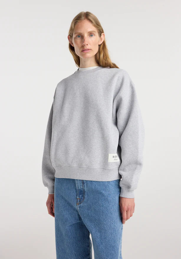 Person wearing a gray sweatshirt and blue jeans on a white background