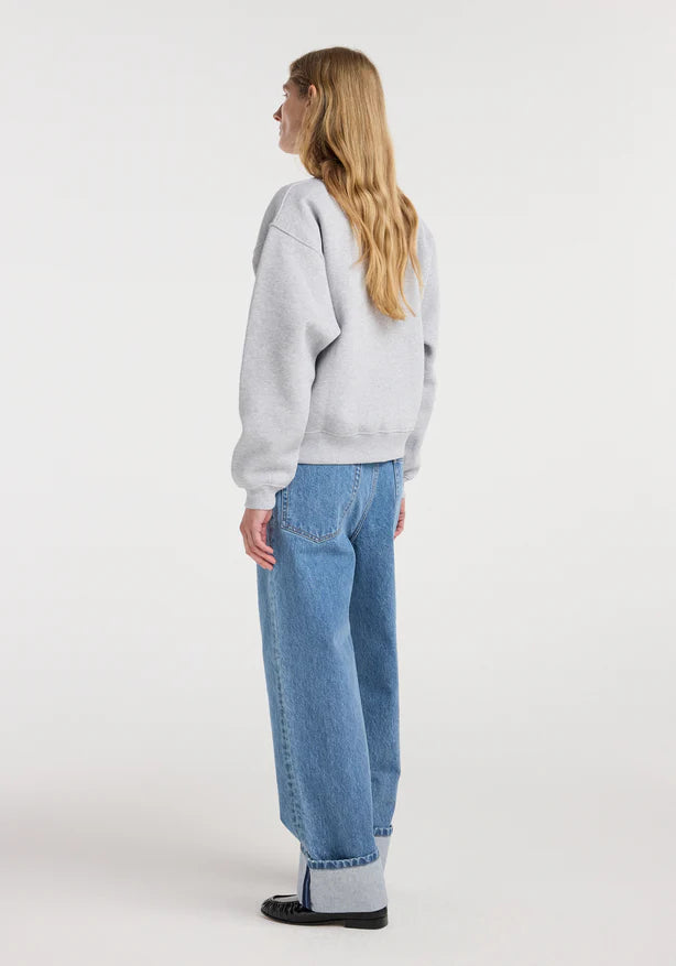 Person wearing a light gray sweatshirt and blue jeans on a white background