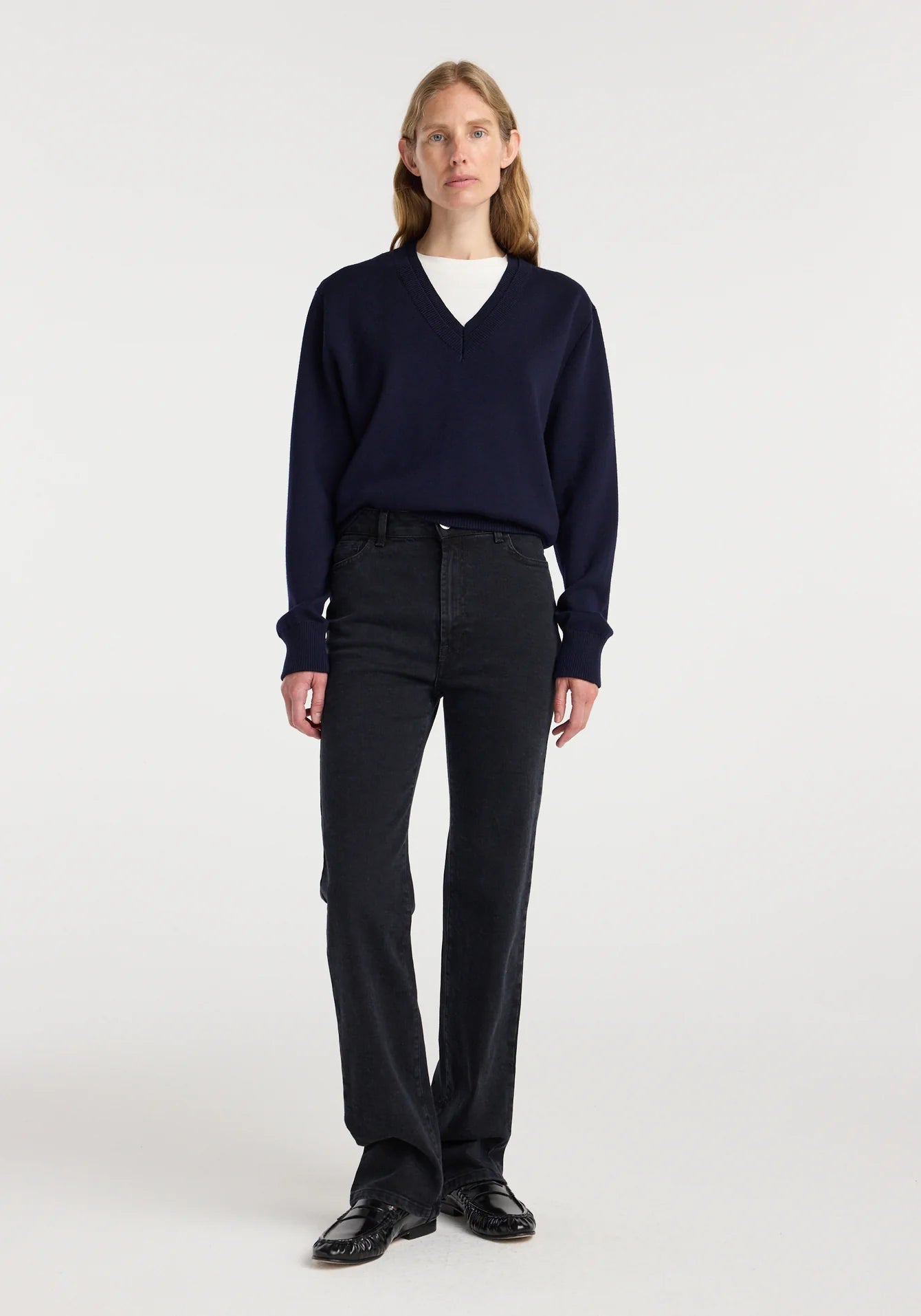 Person wearing a navy sweater and black pants on a white background