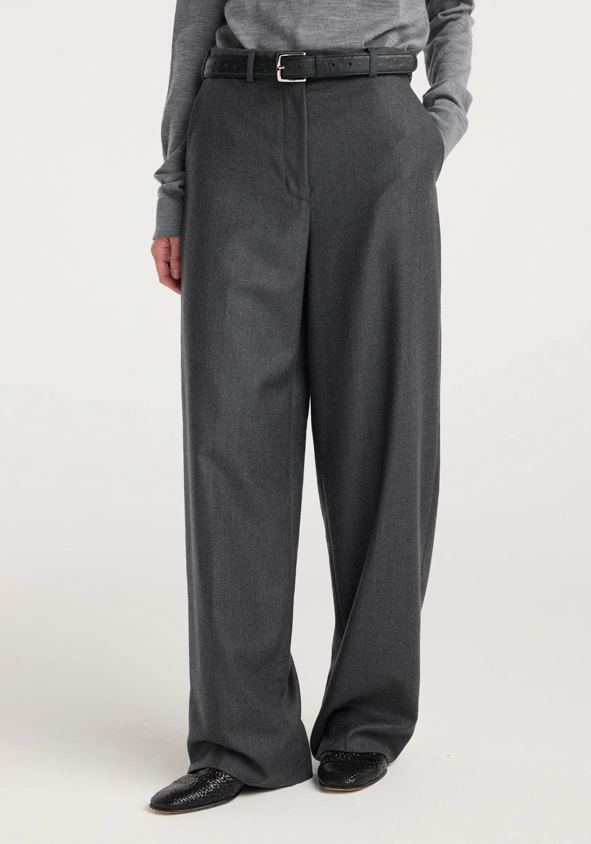 A person wearing dark gray wide-leg trousers with a black belt, paired with a gray long-sleeve top and black shoes, shown from the waist down against a plain light background.