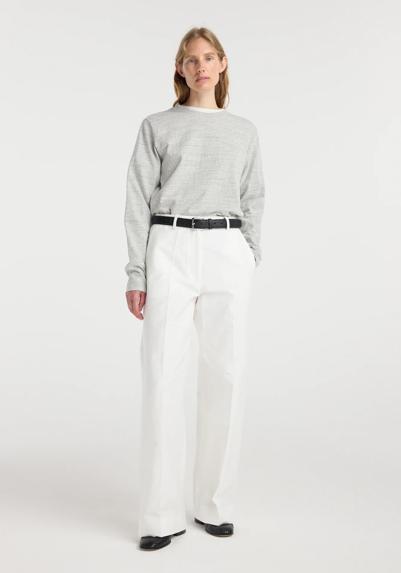 Person wearing a gray sweater and white pants on a white background