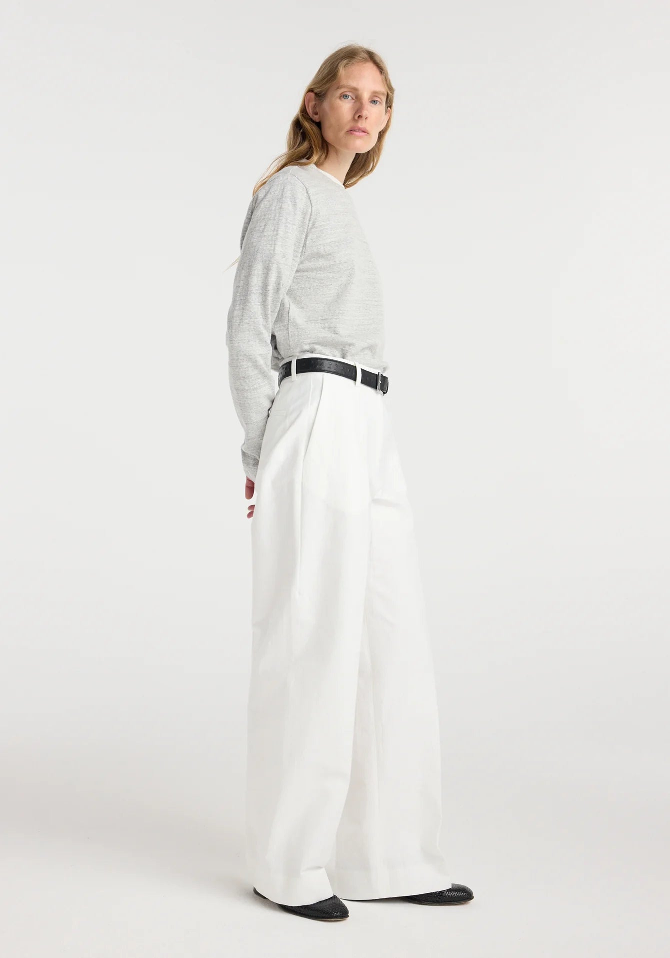 Woman wearing a light gray sweater and white pants on a white background